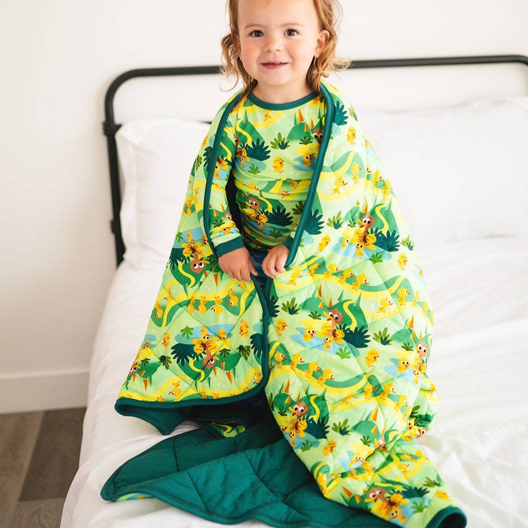 A toddler wrapped in a green quilted blanket with a "5 Little Ducks" print.