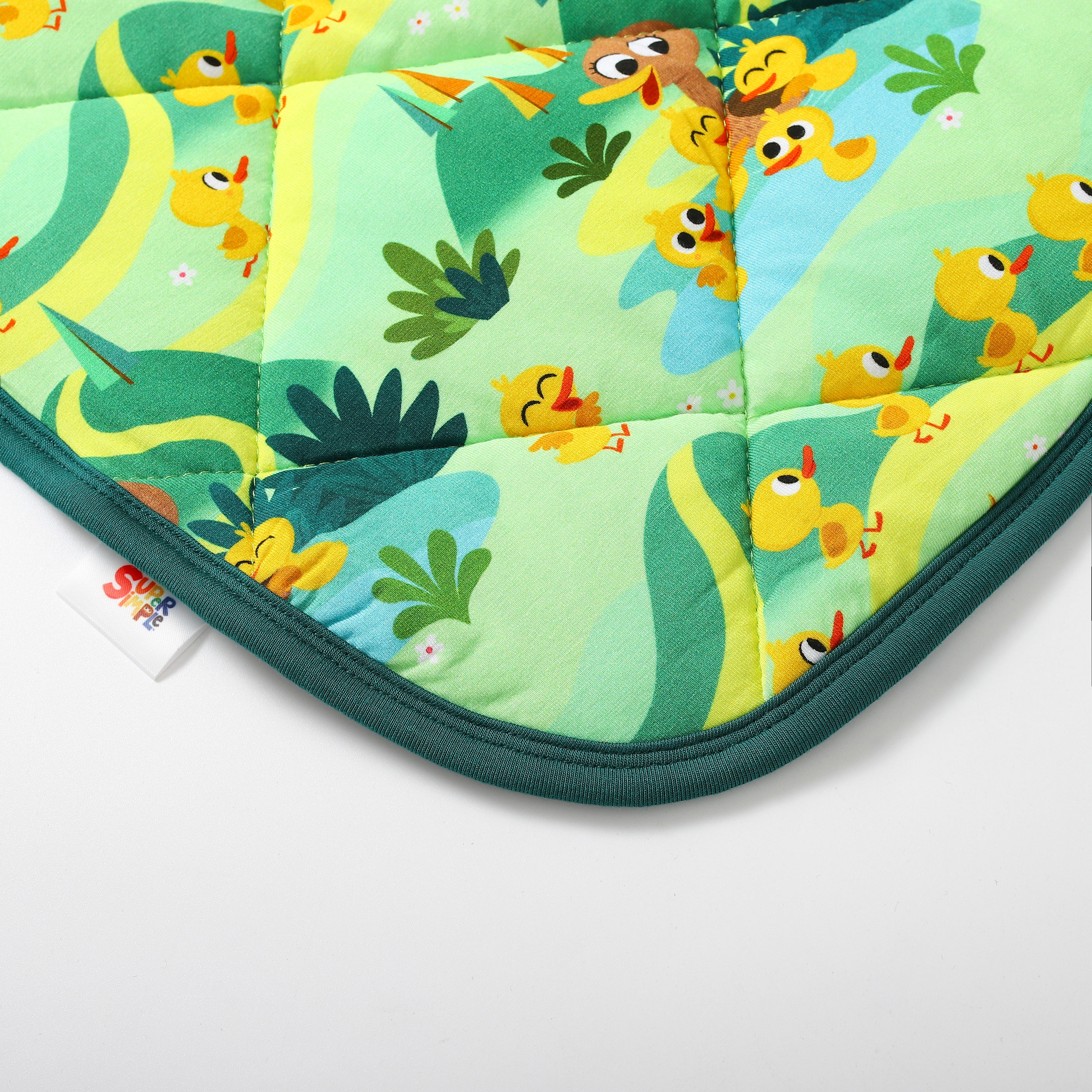 A quilted couch cover with a green and yellow pattern featuring cartoon ducks and plants, with a white tag that says "SUPER SIMPLE".