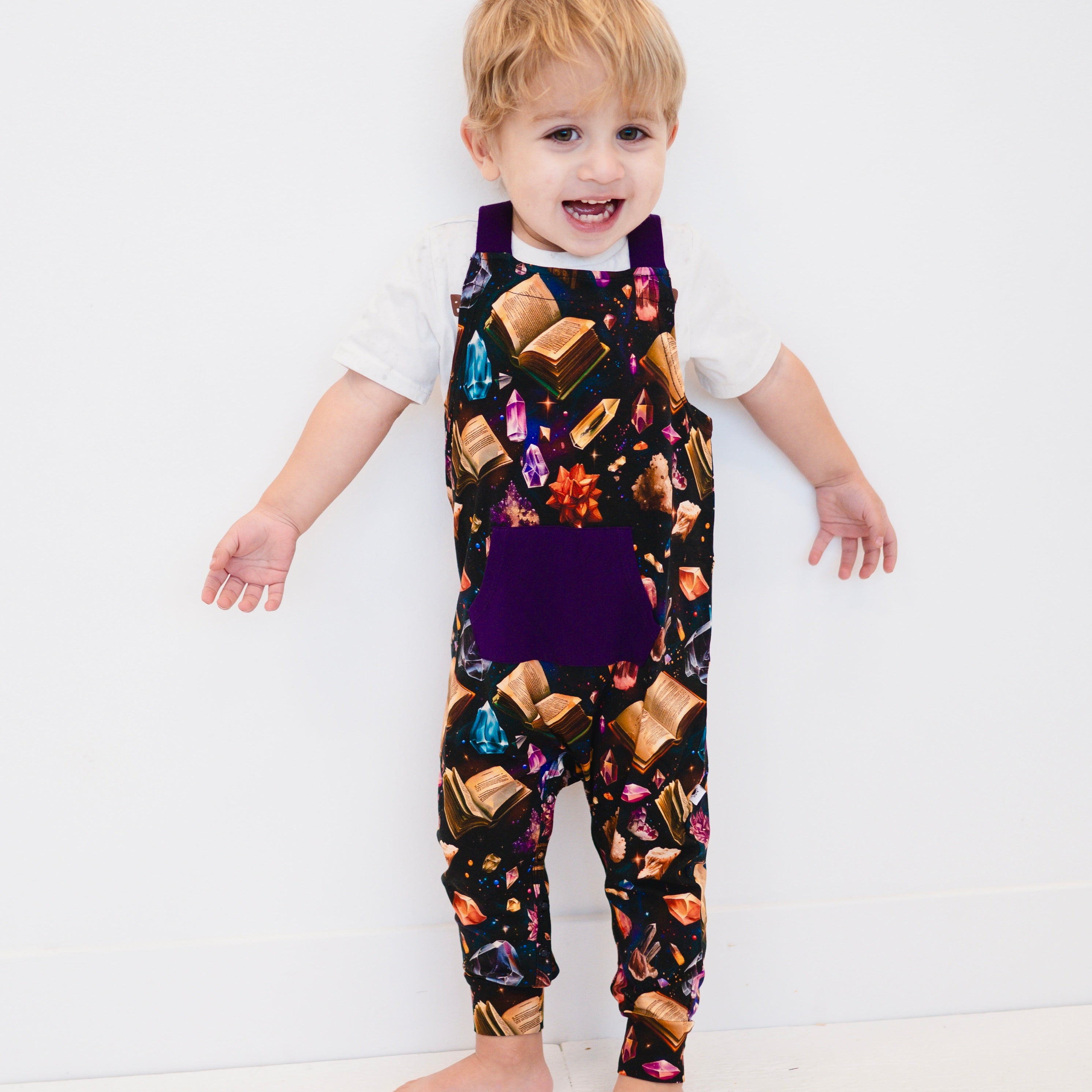 Toddler overalls with a crystal and book print and a purple pocket.