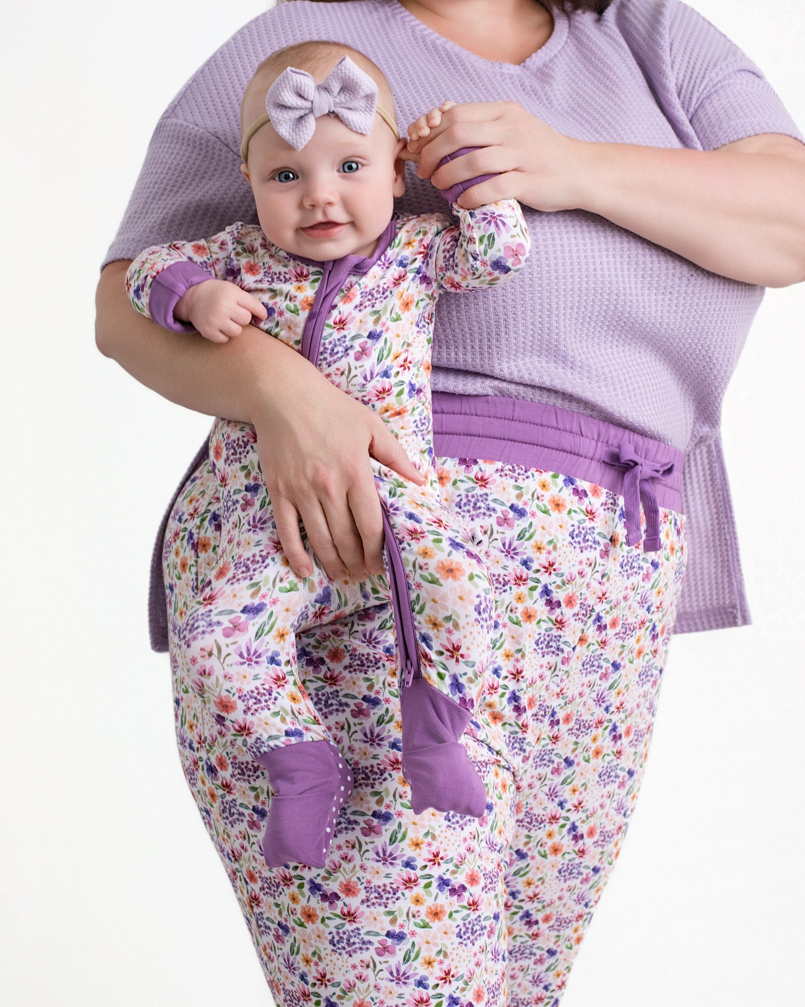 A baby wearing a floral print bamboo pajama set with a purple bow headband.