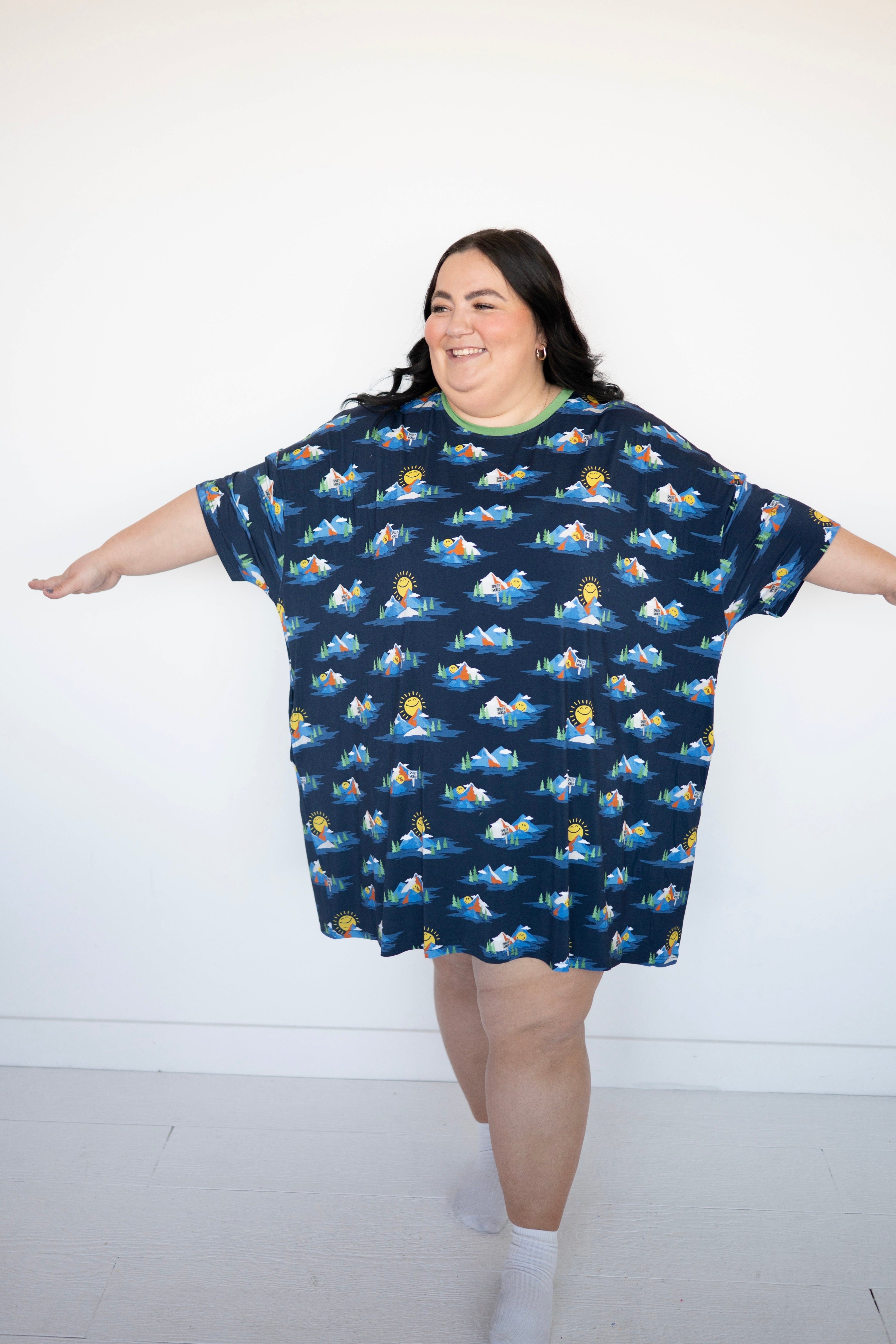 A woman wears a navy blue oversized t-shirt with a repeating print of mountains, trees, and smiling suns.