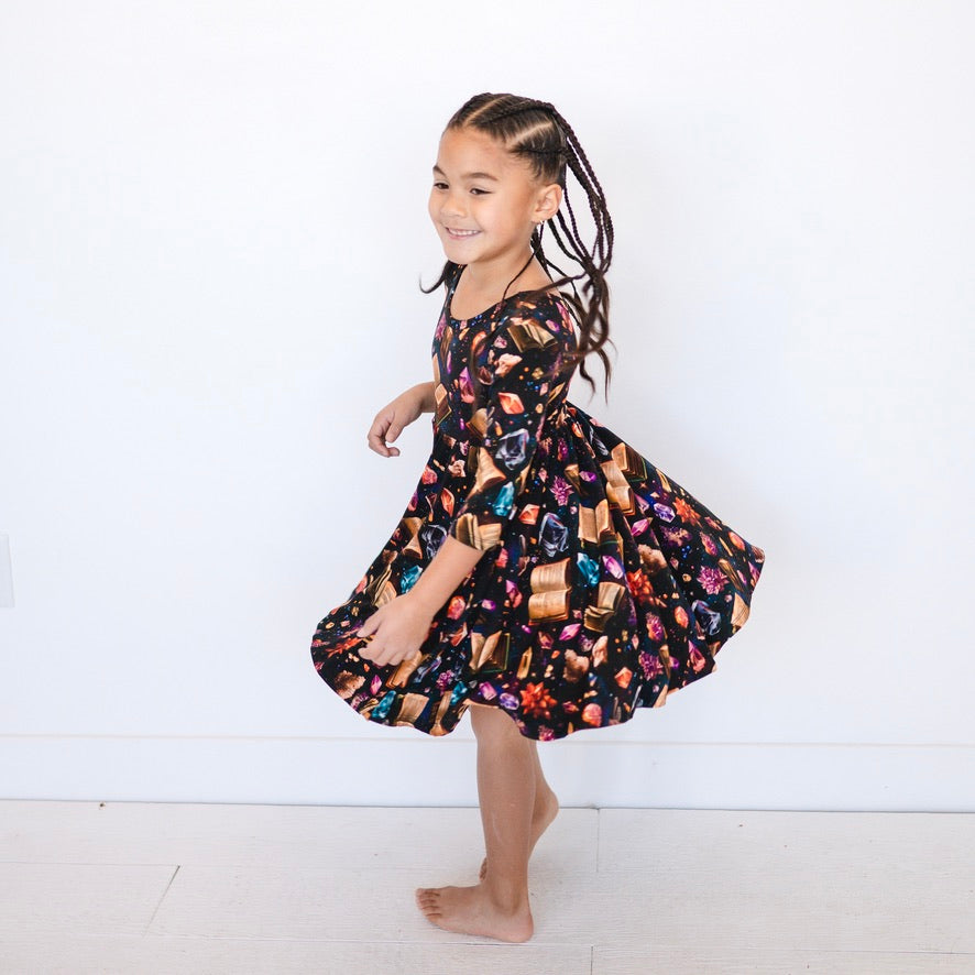 A girl in a black dress with a crystal and book print twirls.
