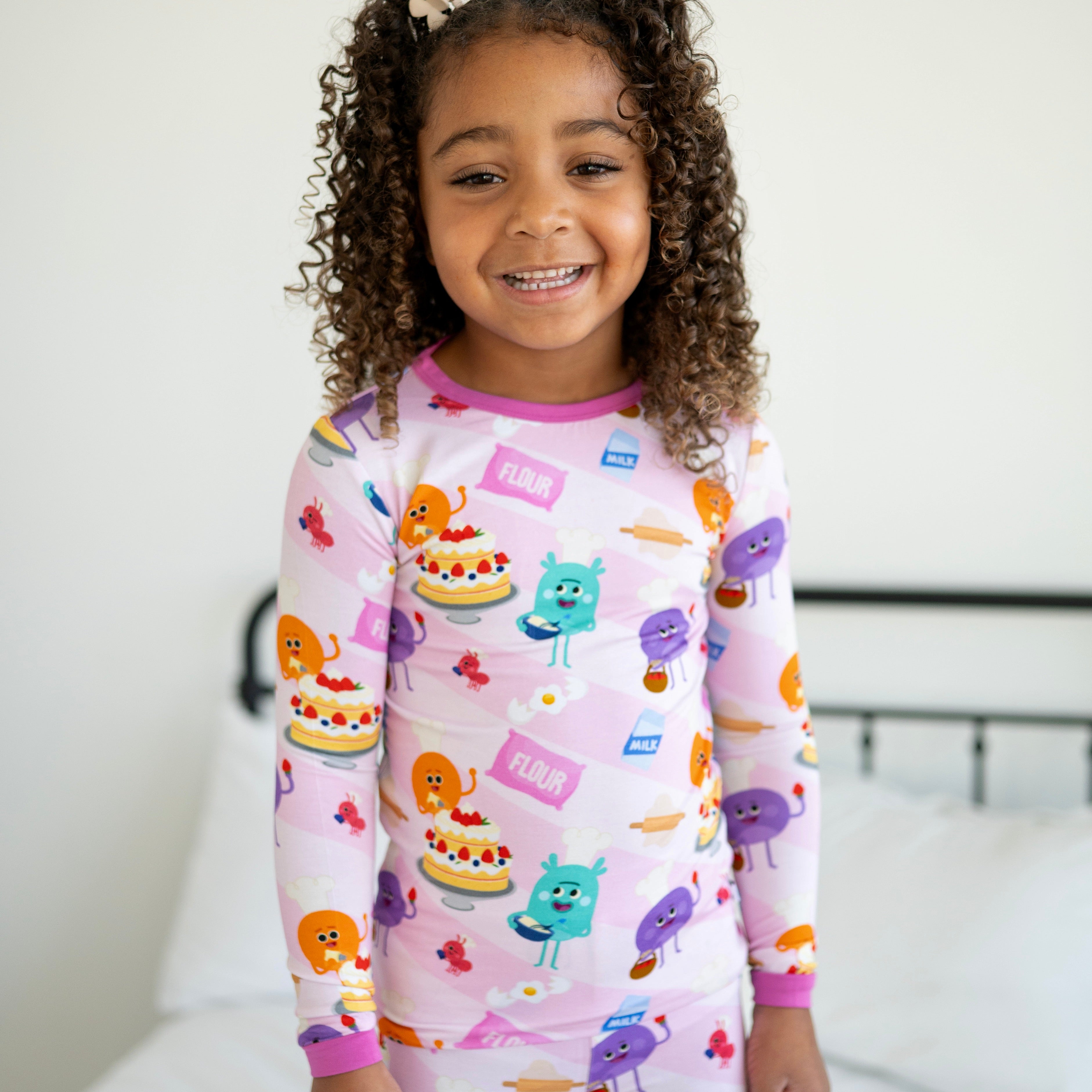 A young girl smiles in pink pajamas with a baking-themed print.