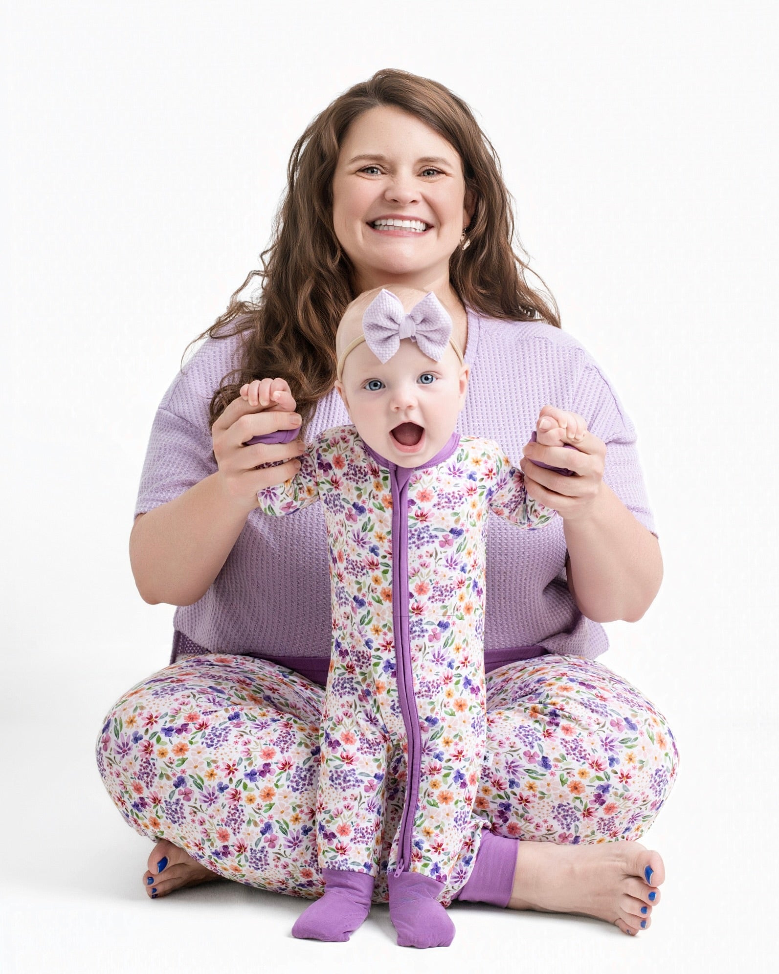 A woman and baby in matching floral pajamas sit on a white background.