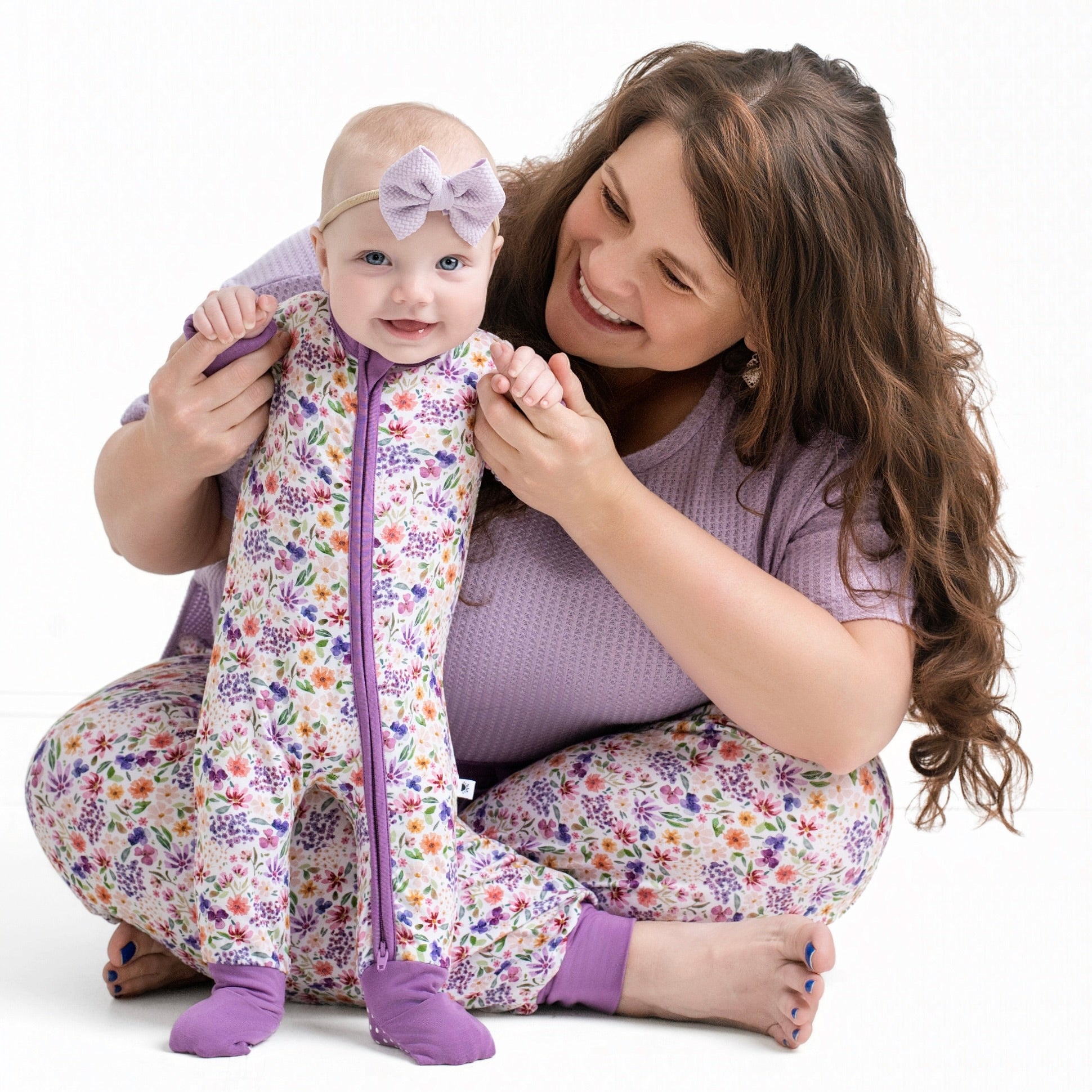 A baby in a floral zip-up sleeper and a woman in matching pajamas.
