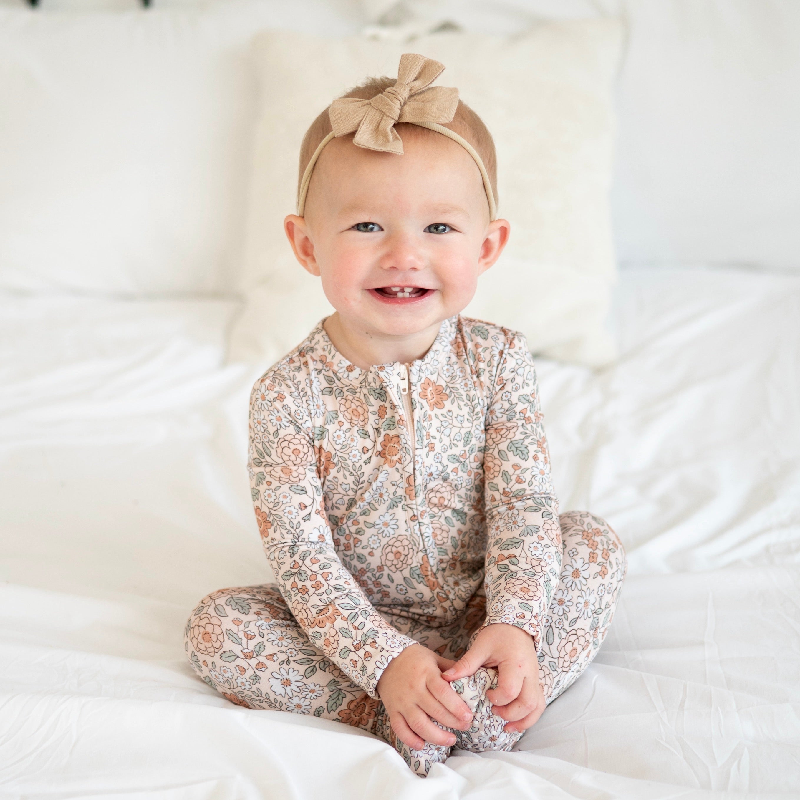 Baby in a vintage floral zip pajama set with a tan bow headband.