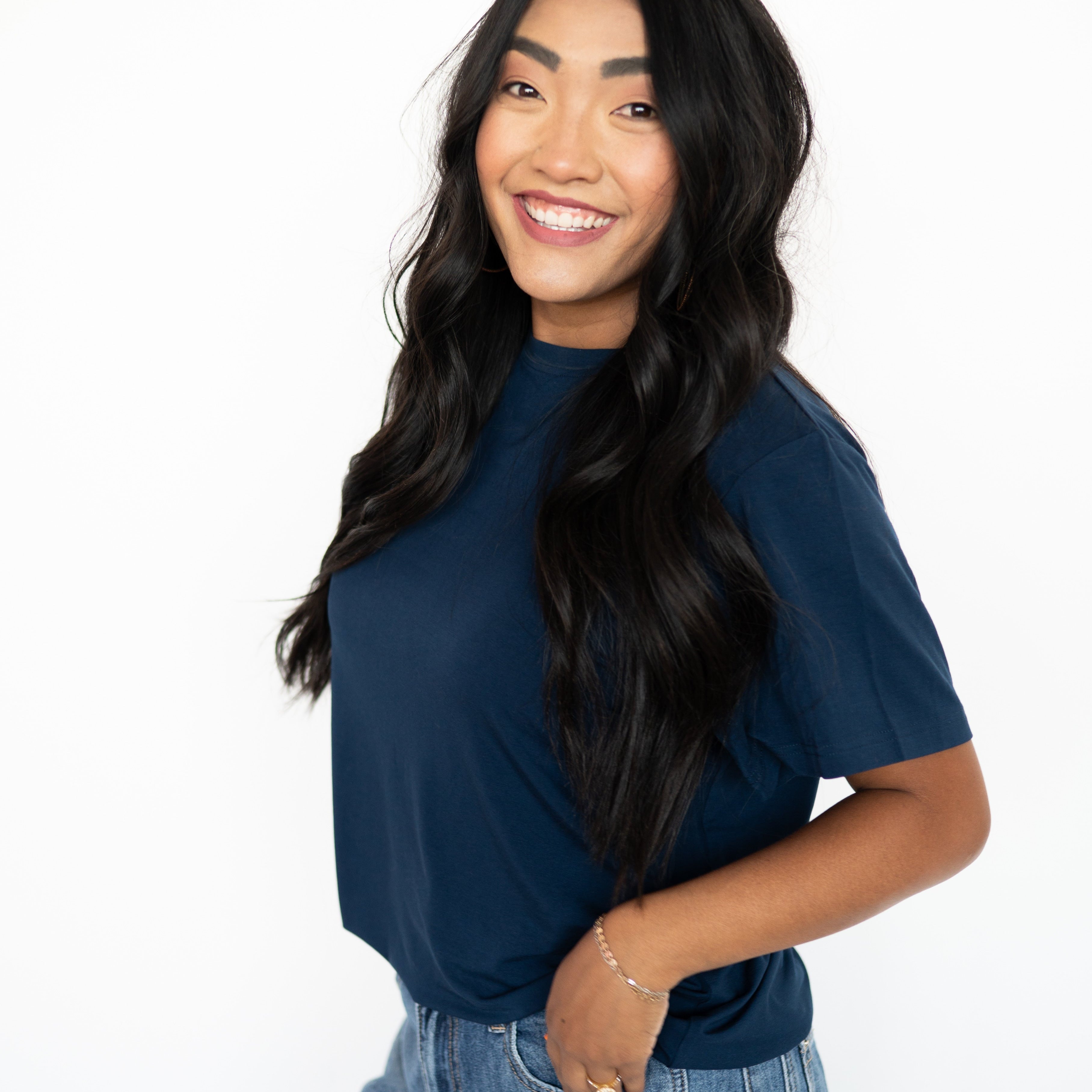 A woman smiles wearing a navy oversized bamboo t-shirt and jeans.
