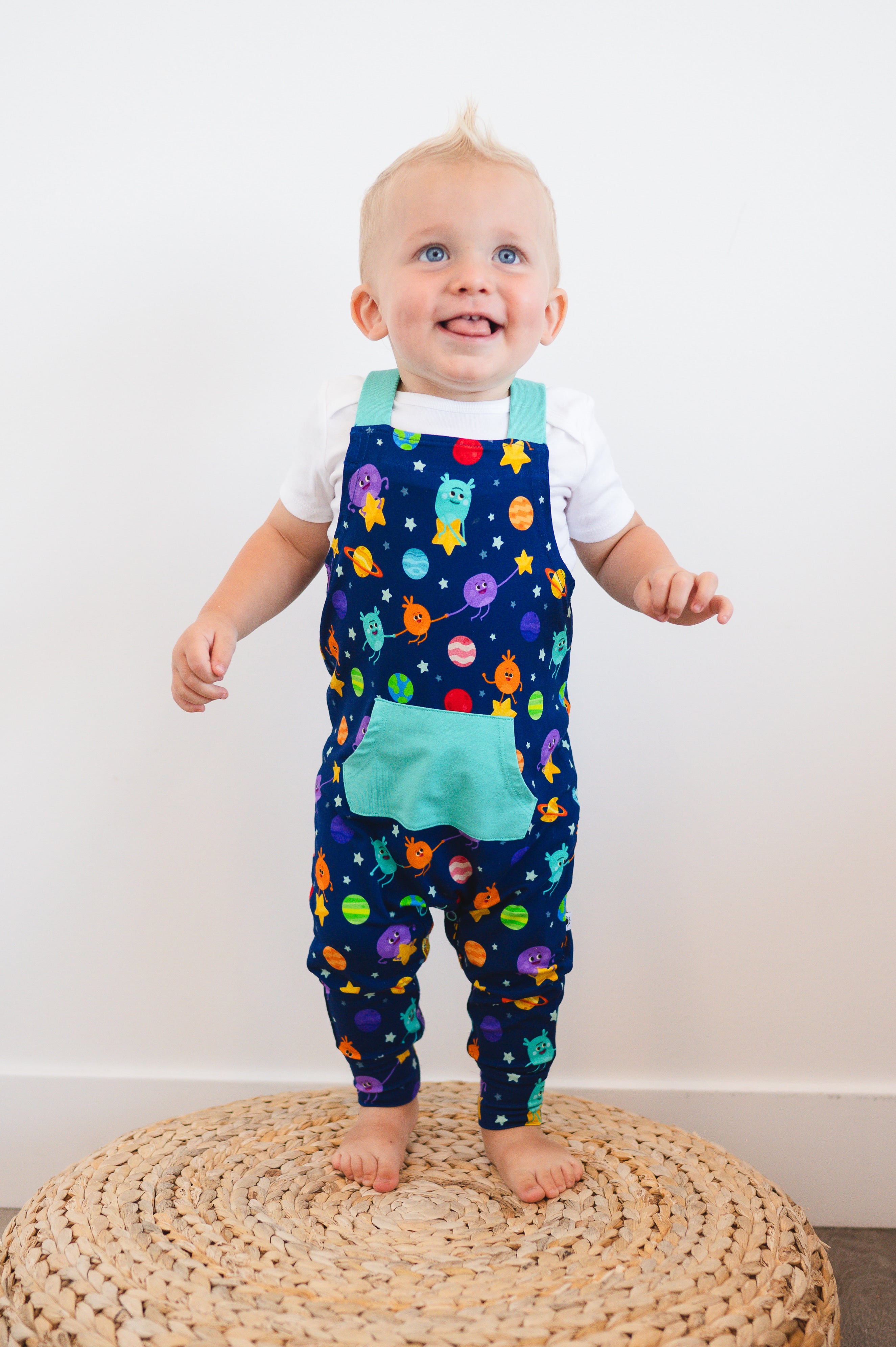 A baby boy wears blue overalls with a space-themed print.