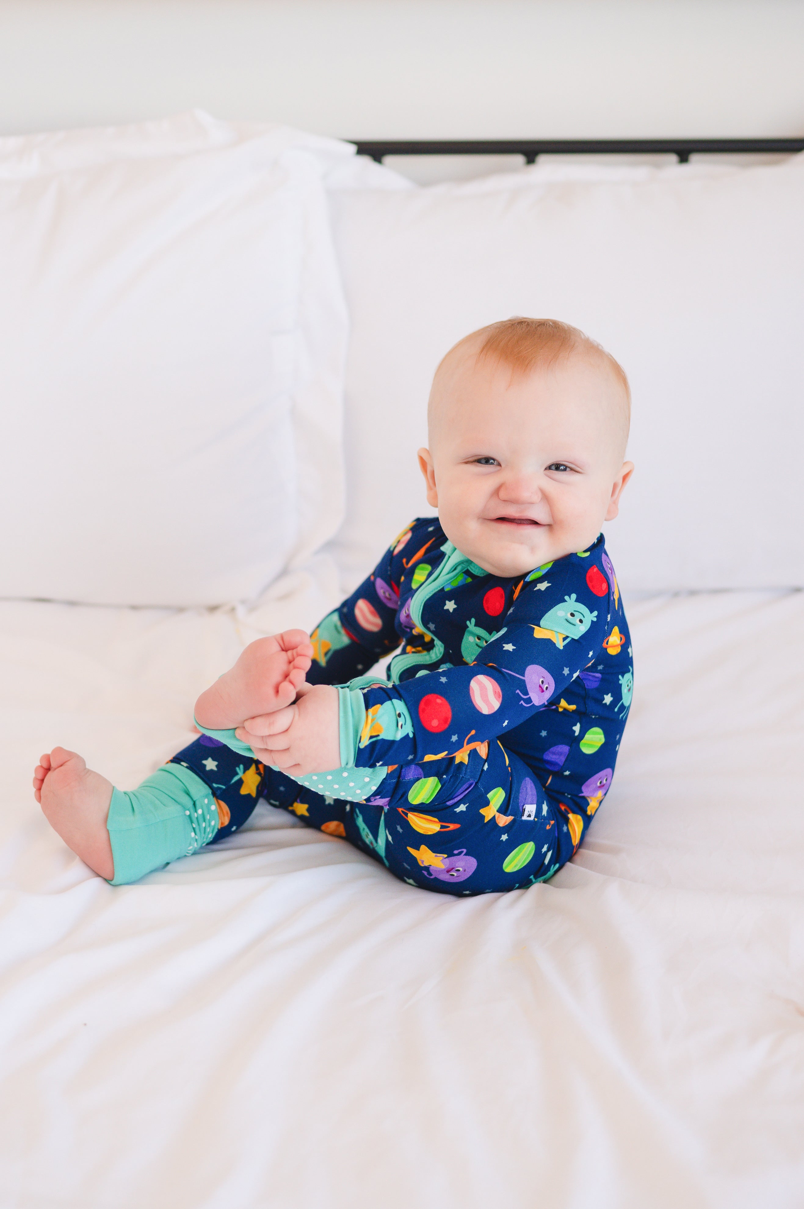 A baby in a navy blue pajama set with a space-themed print of aliens and planets.