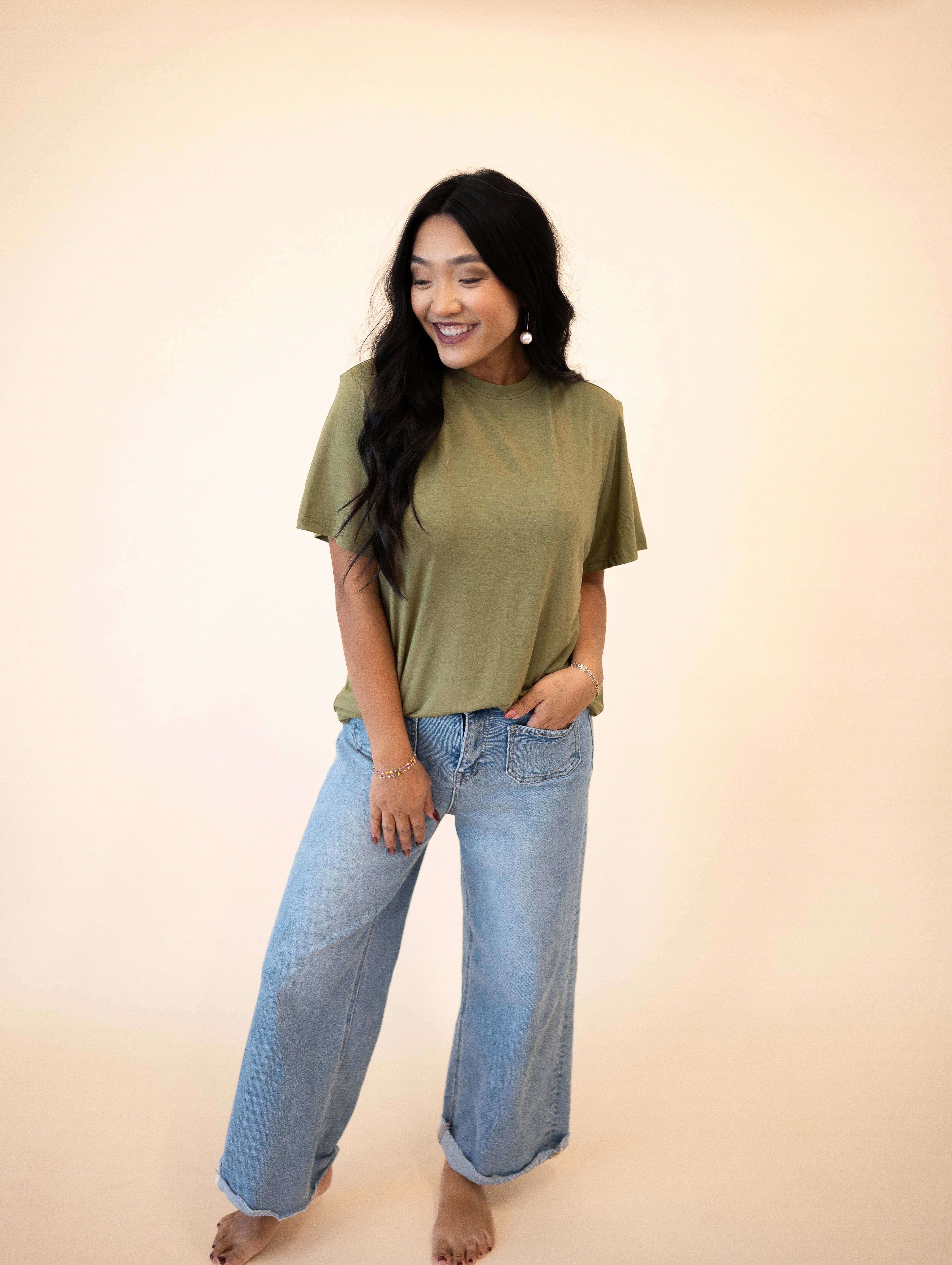 A woman wears an olive green oversized tencel modal tee and light wash wide-leg jeans.