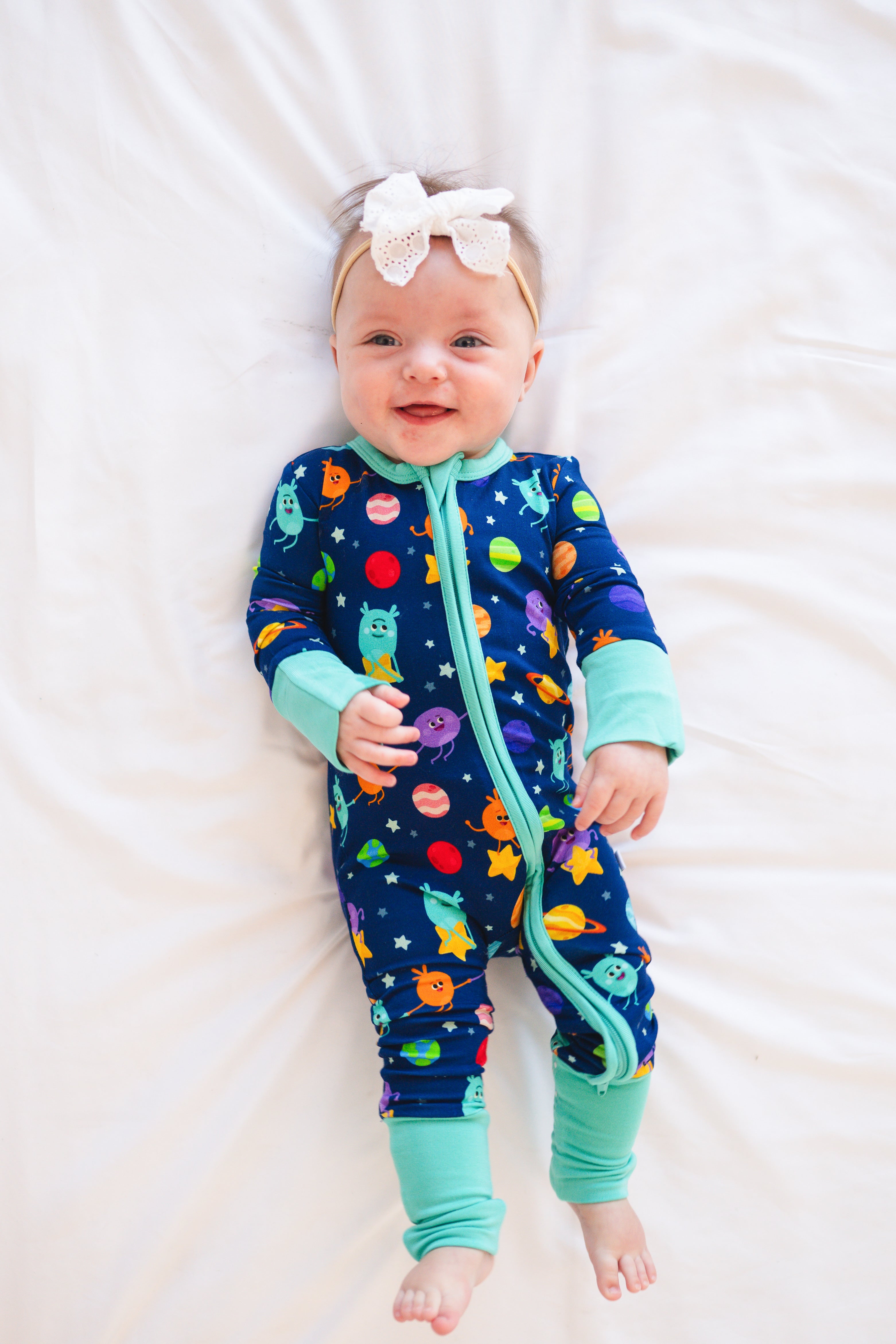 A baby wearing a blue pajama set with a space-themed Bumble Nums print and a white bow.