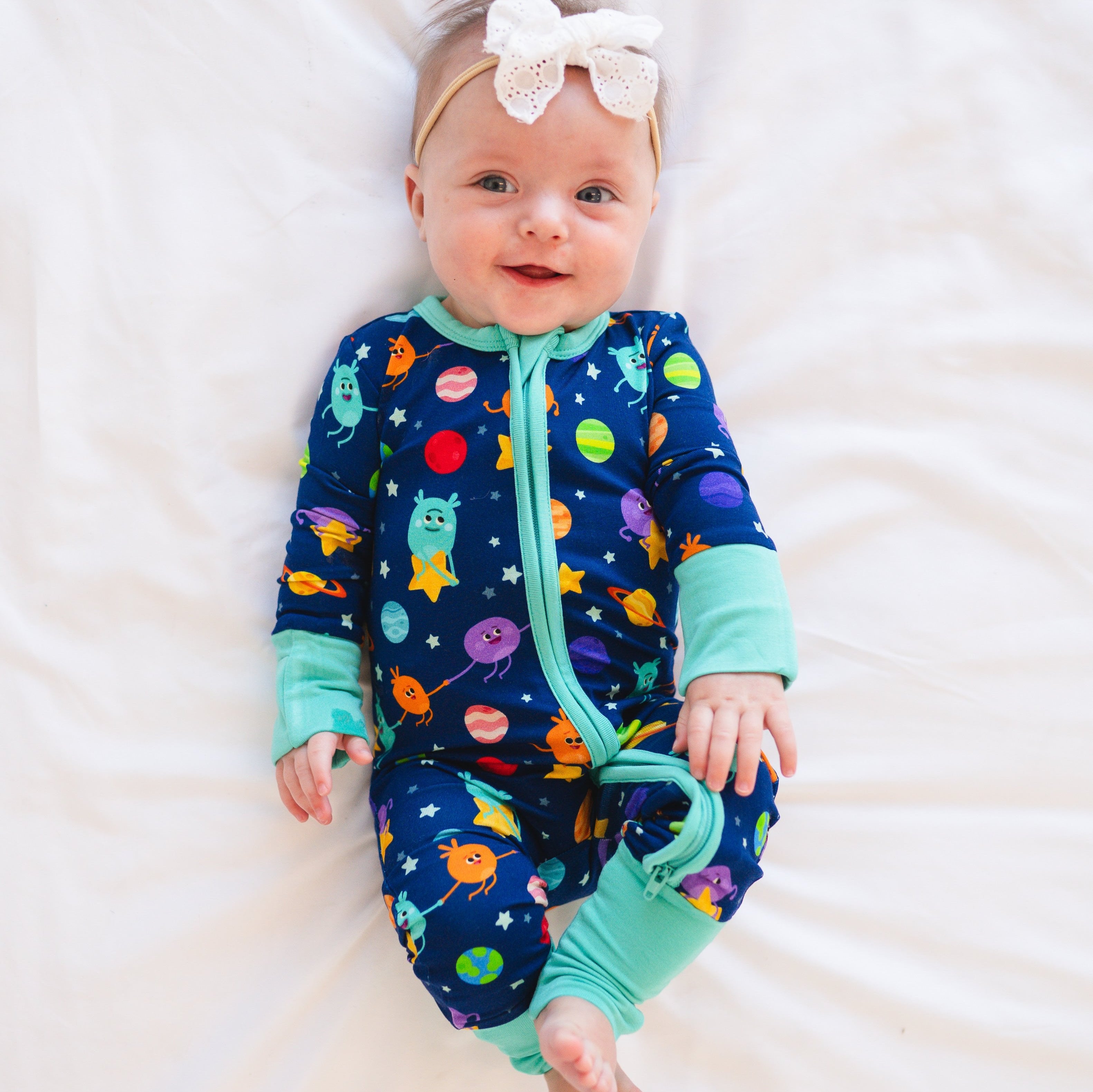 Baby in a navy blue pajama set with a space-themed print and a white bow headband.