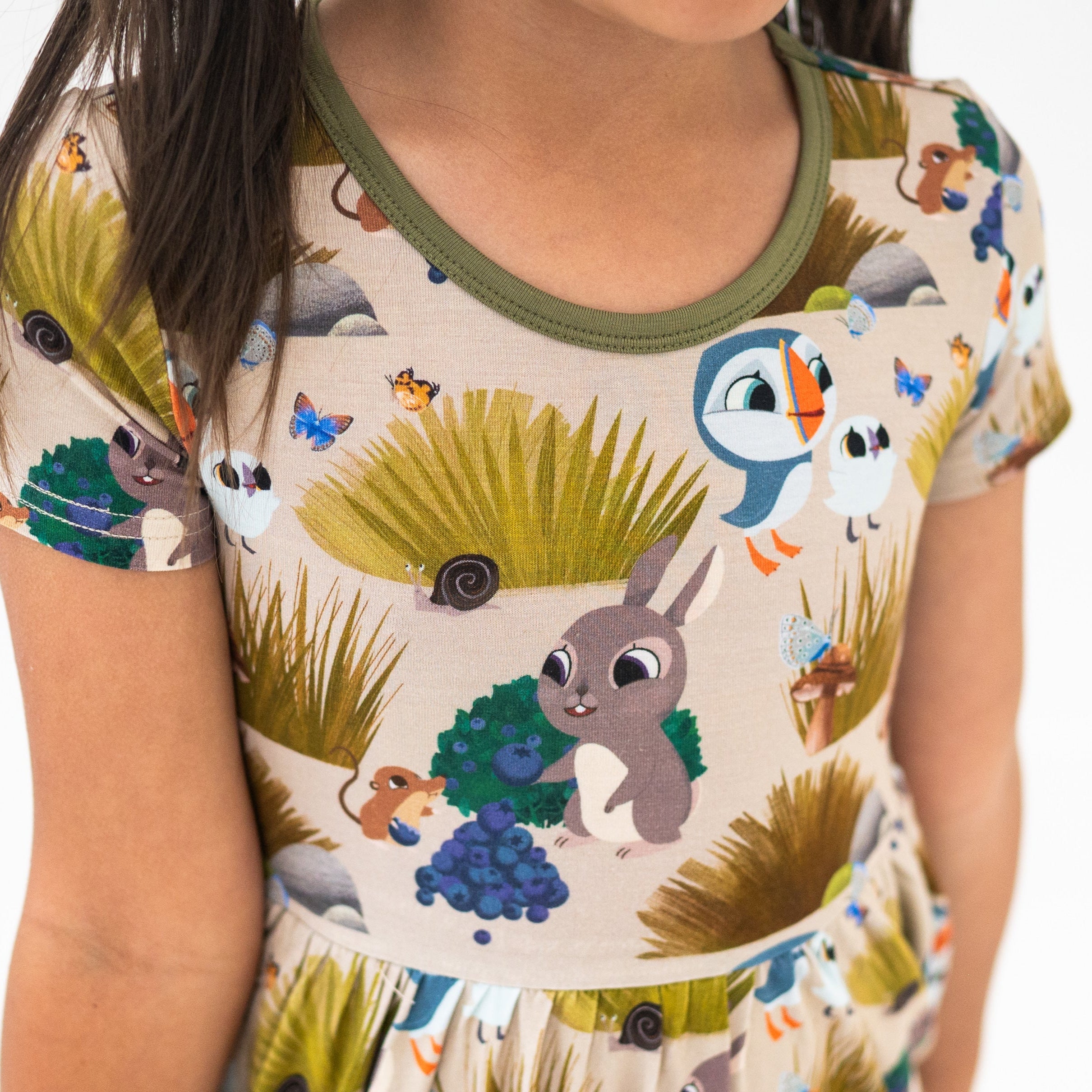 A child wears a tan dress with a Puffin Rock™ woodland print.