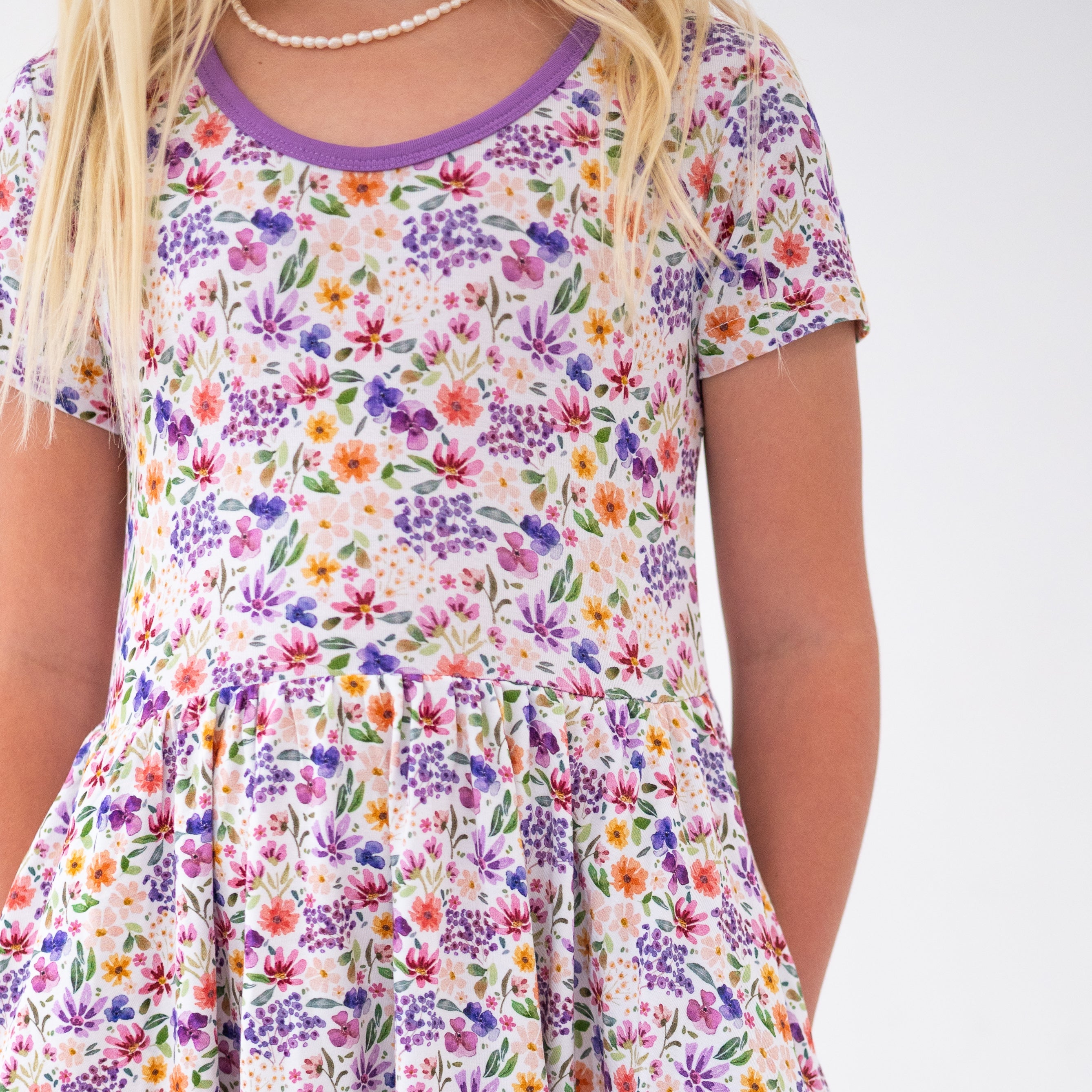 A girl wears a white dress with a dainty floral print and a purple neckline.