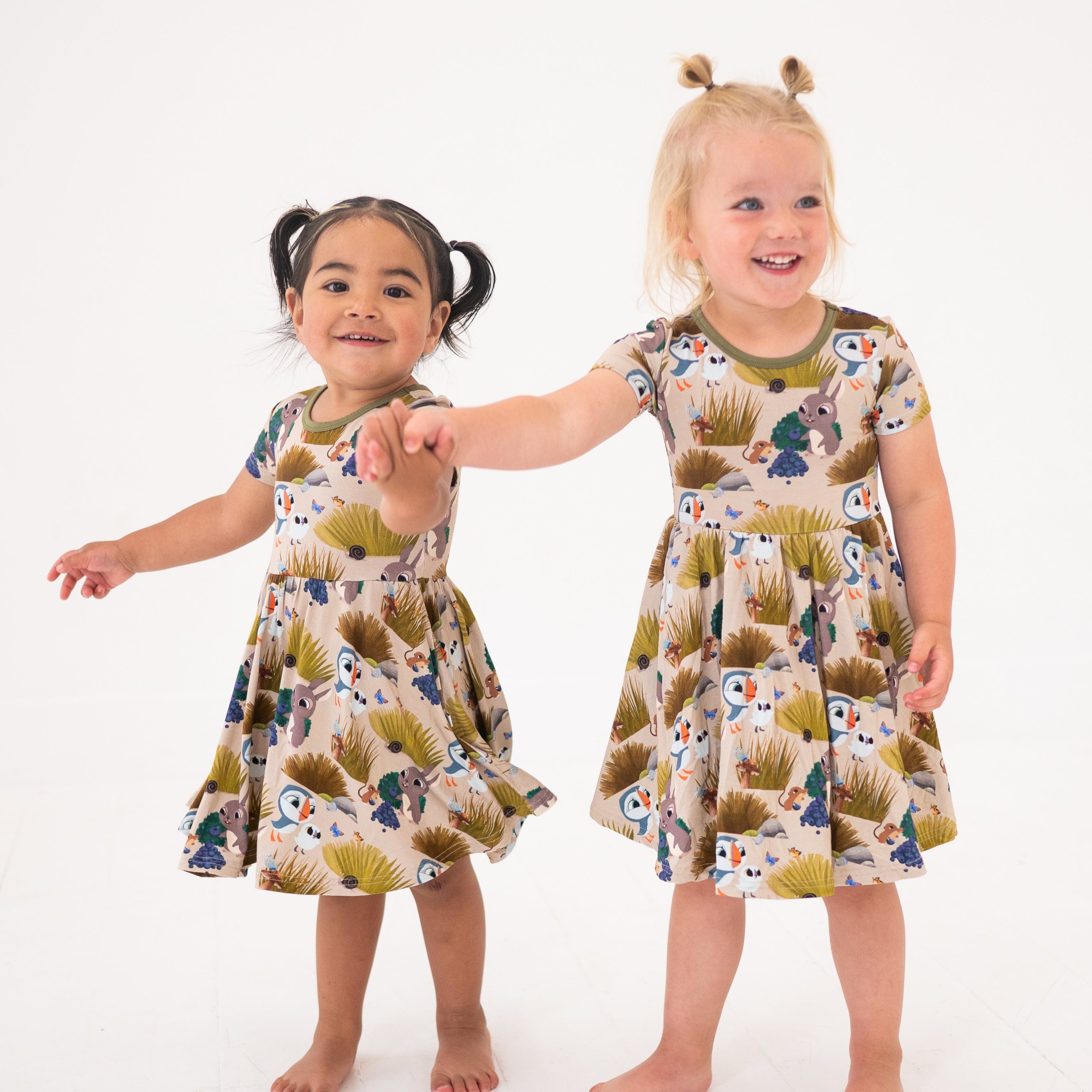 Two young girls in matching Puffin Rock™ bamboo dresses with a woodland print.