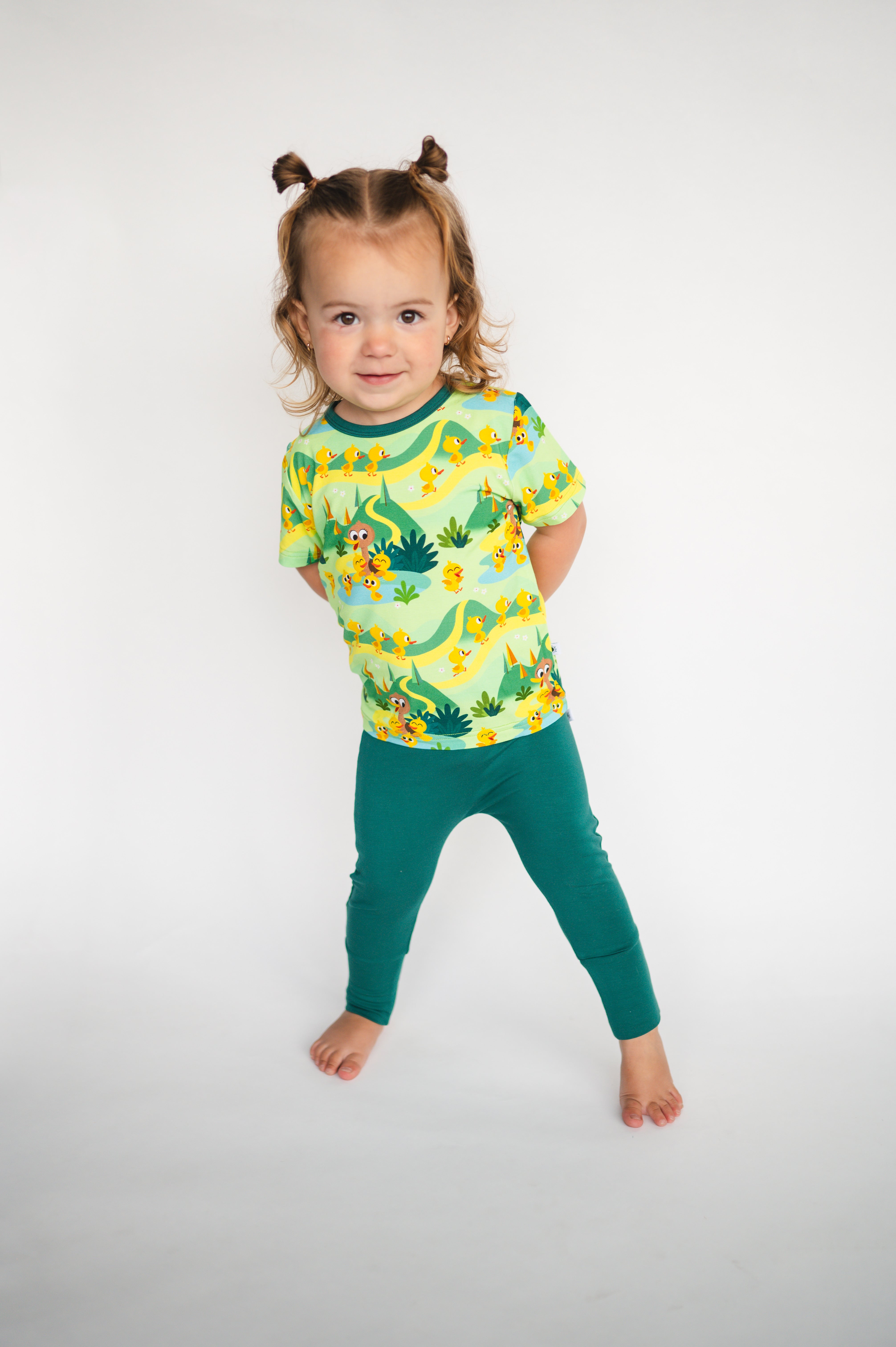 A young child wears a green duck pond print shirt and green pants.