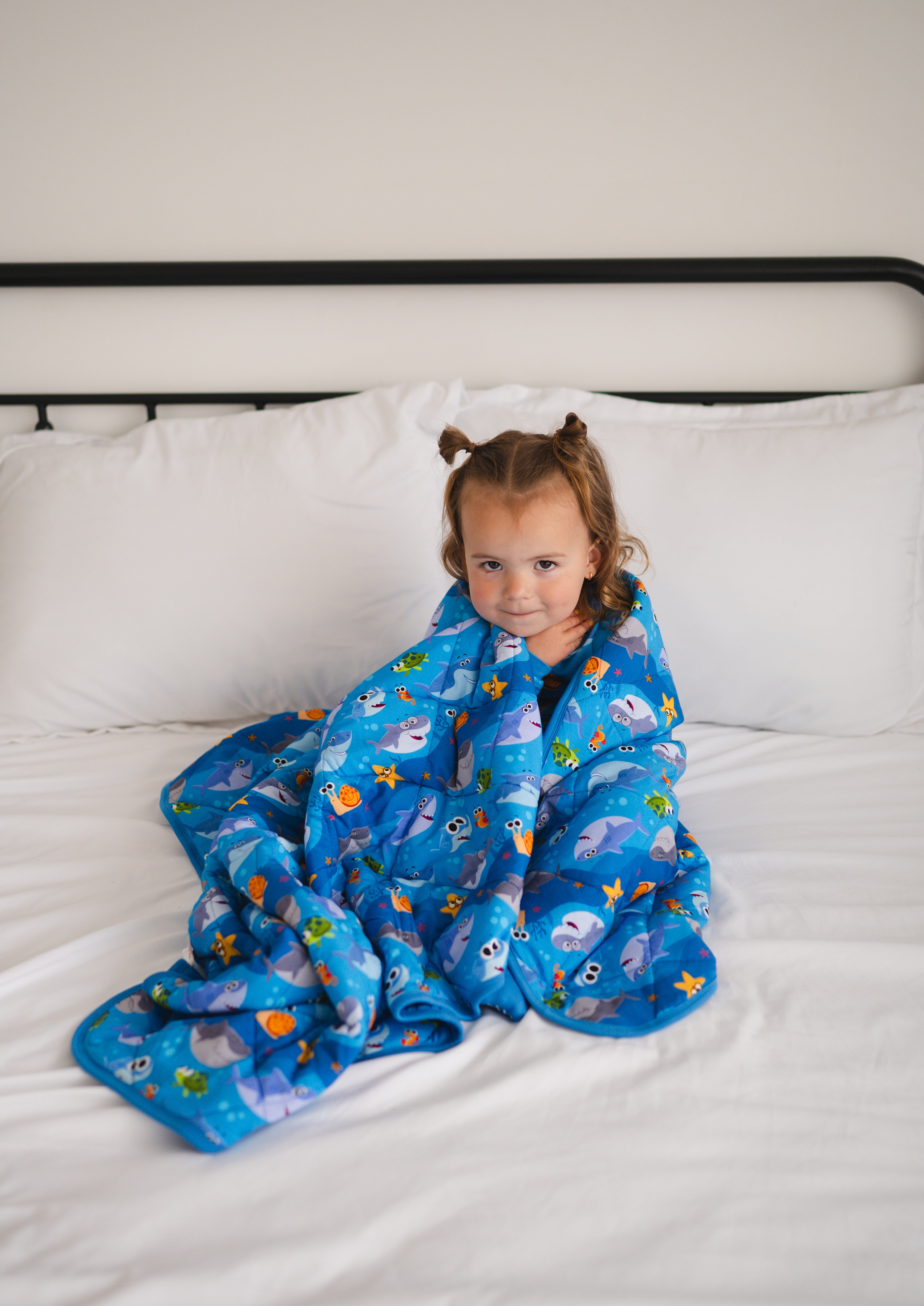 A young girl is wrapped in a blue blanket with a Baby Shark pattern.
