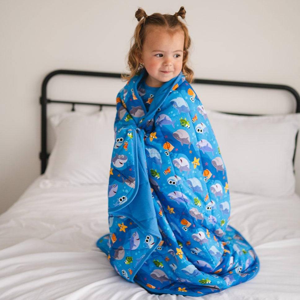 A young child wrapped in a blue blanket with a Baby Shark print.