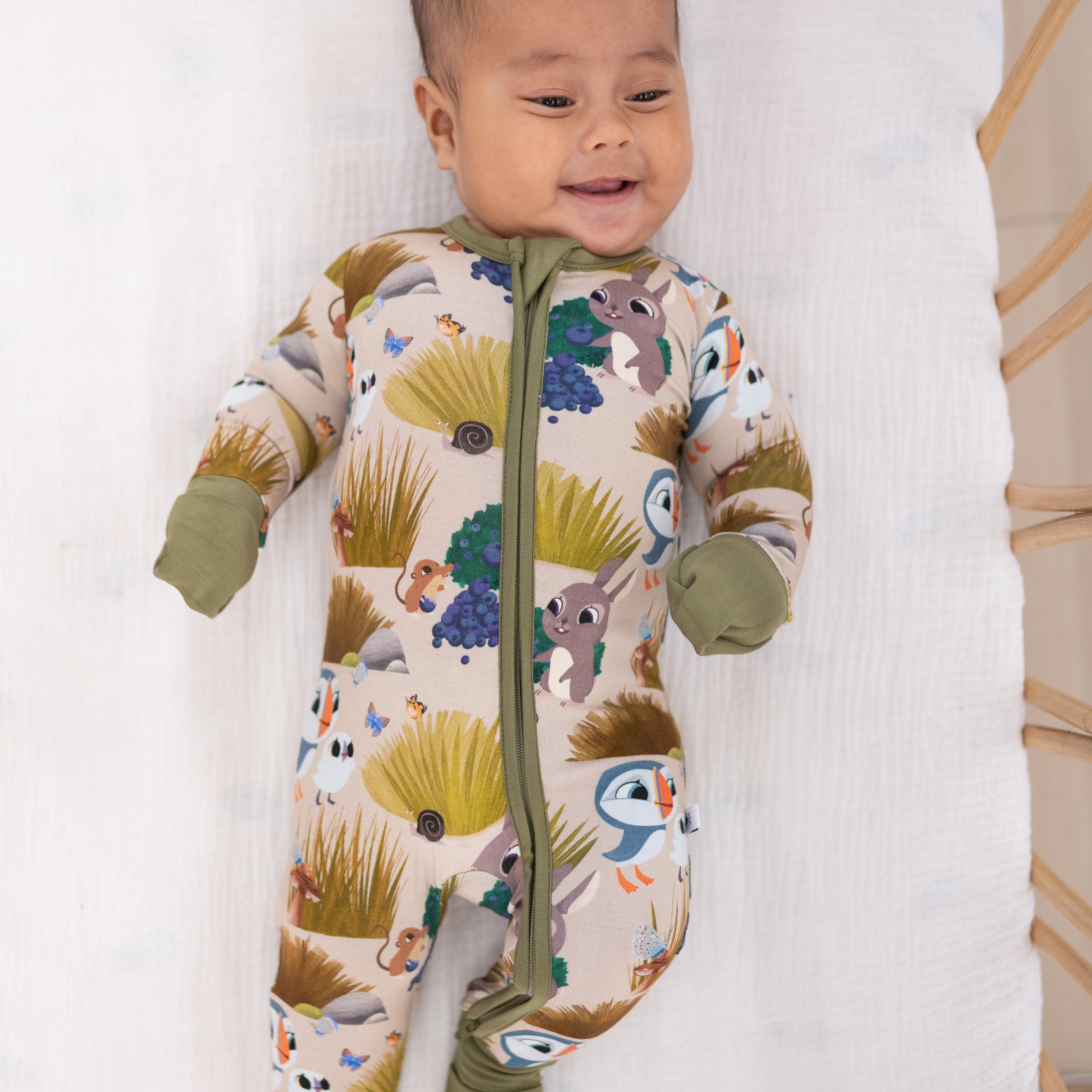 A baby smiles in a tan bamboo pajama set with a Puffin Rock print.