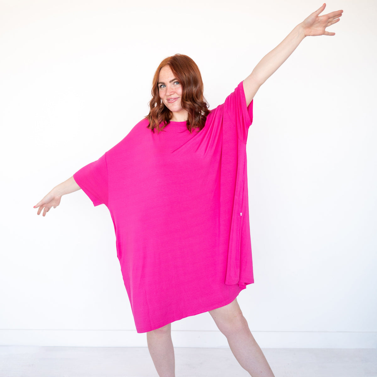 A woman in a bright pink oversized sleep tee with her arms outstretched.