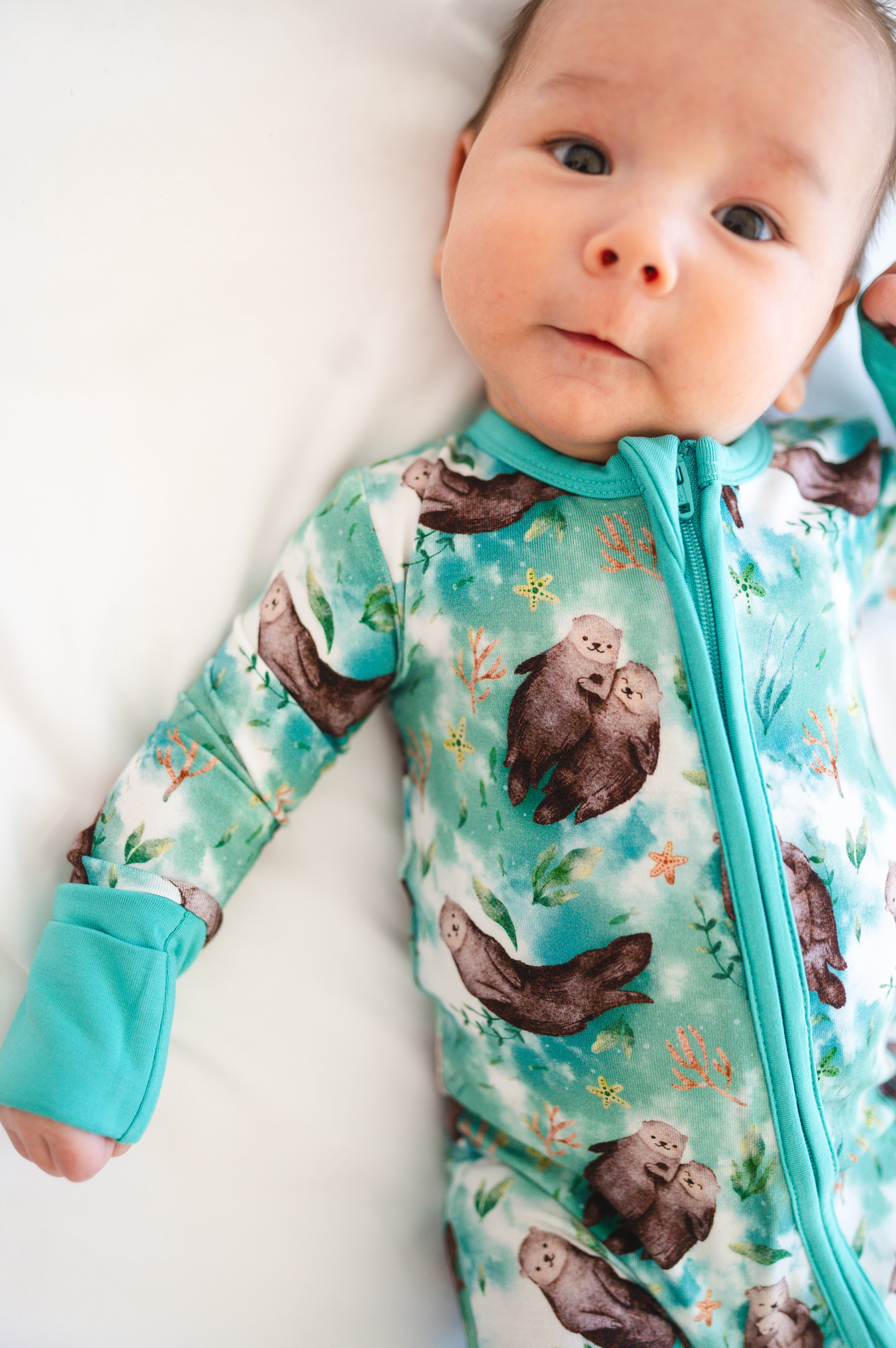 A baby wears a teal pajama with an otter print.