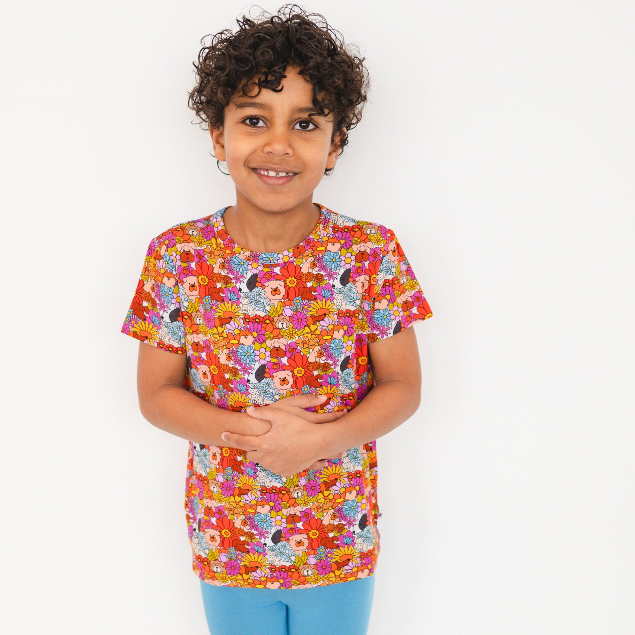 A young boy smiles wearing a colorful t-shirt with a floral and dog print.