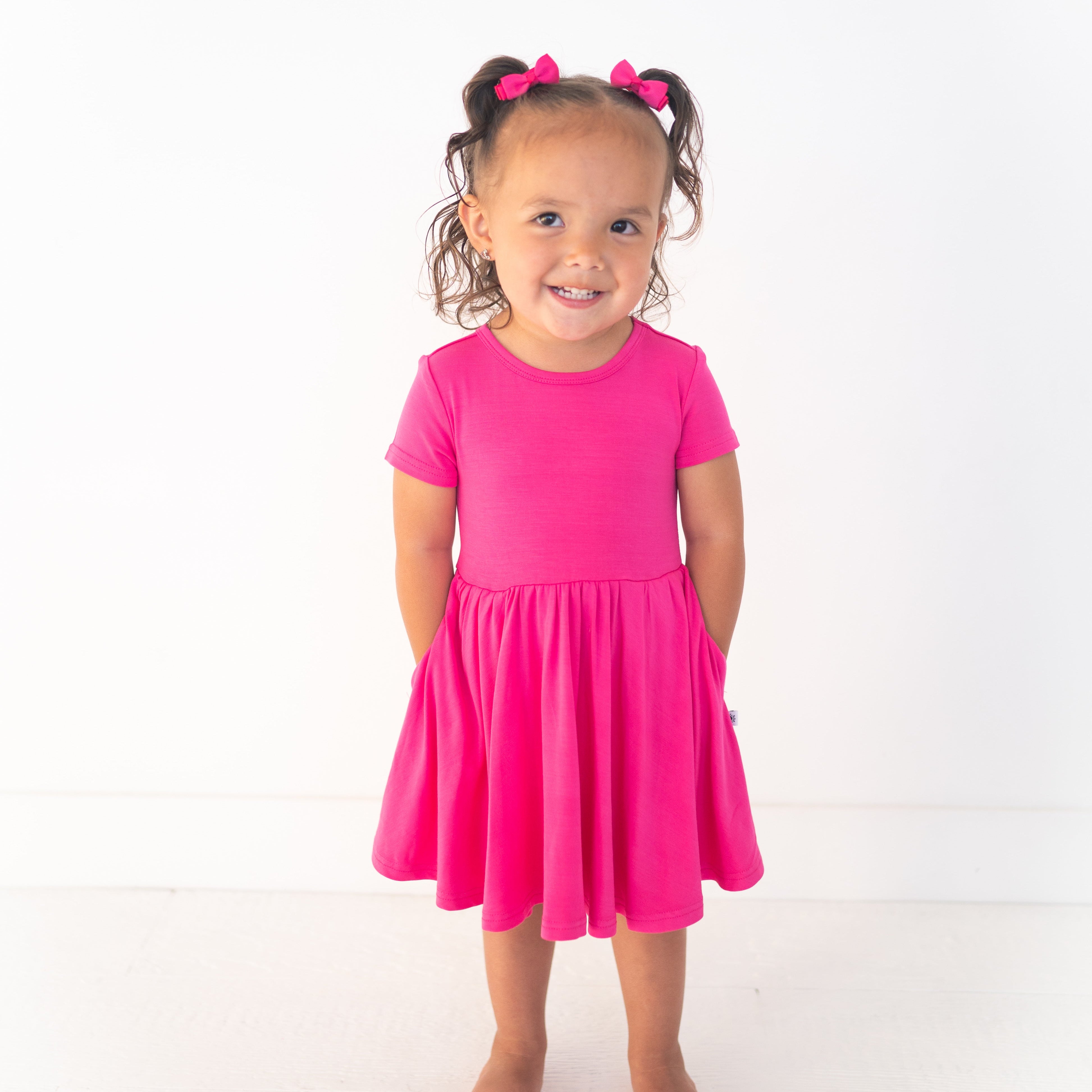 A young girl wears a bright pink bamboo dress with pockets.