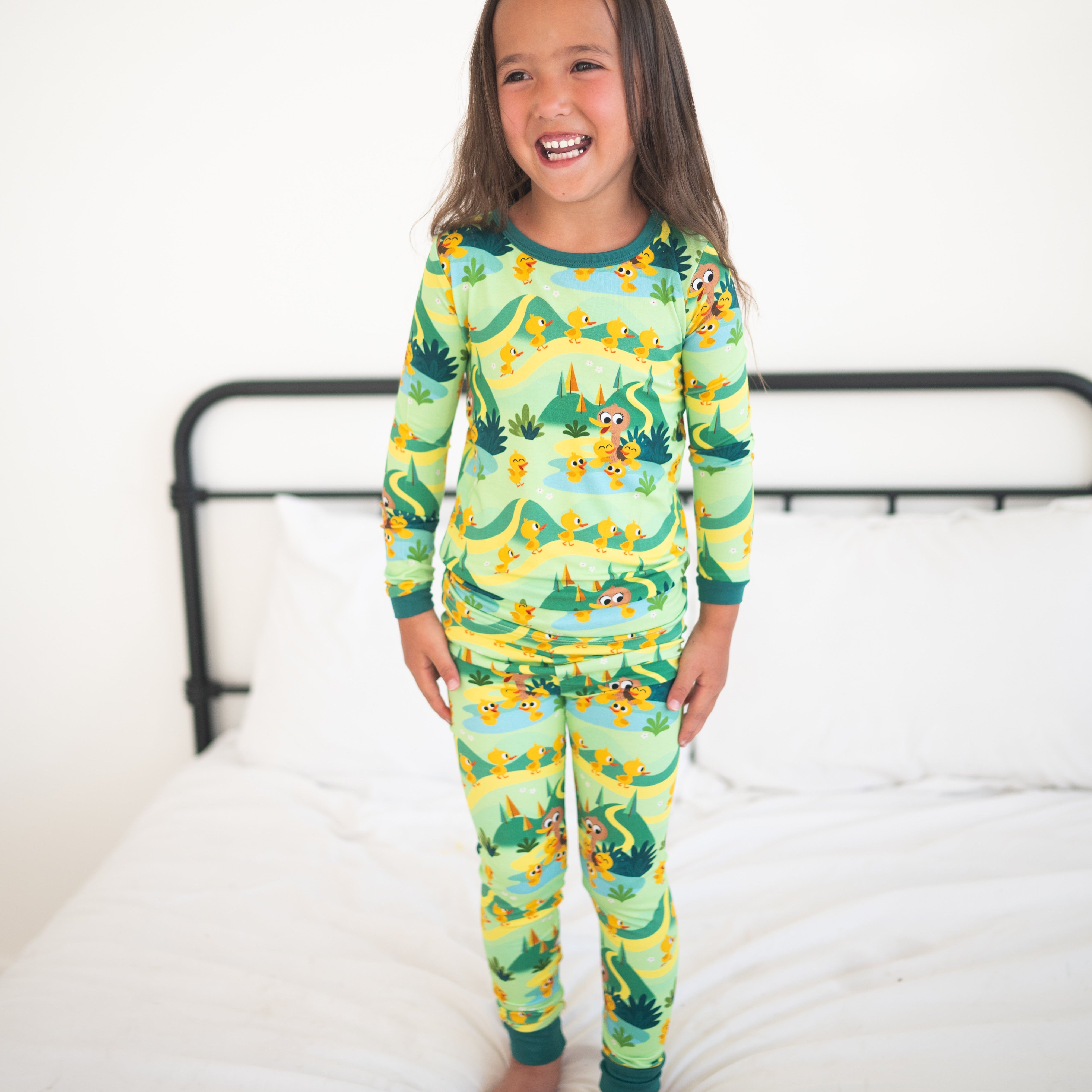 A young girl smiles while wearing a green pajama set with a duckling print.