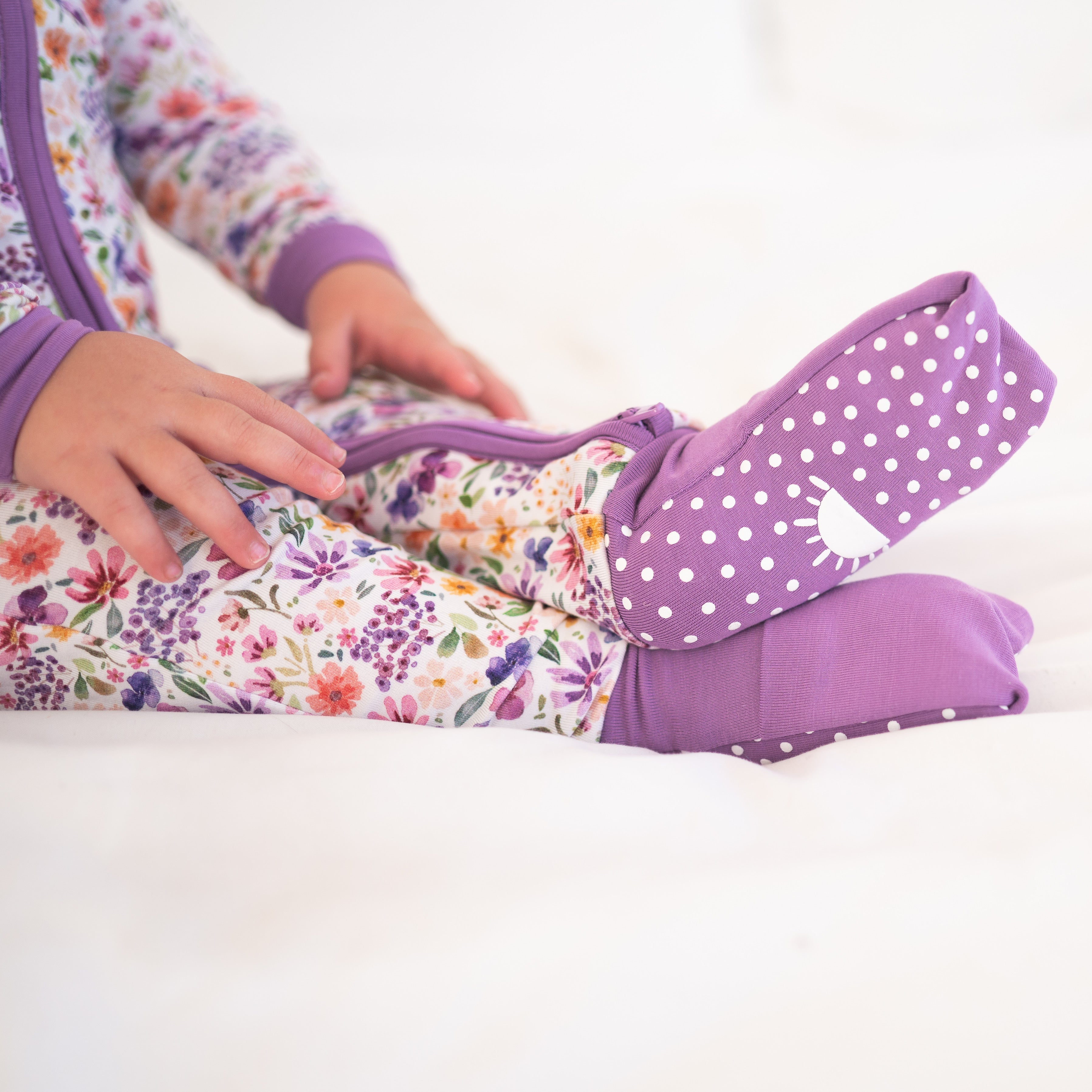 A baby wearing a floral print bamboo sleeper with purple polka dot footies.