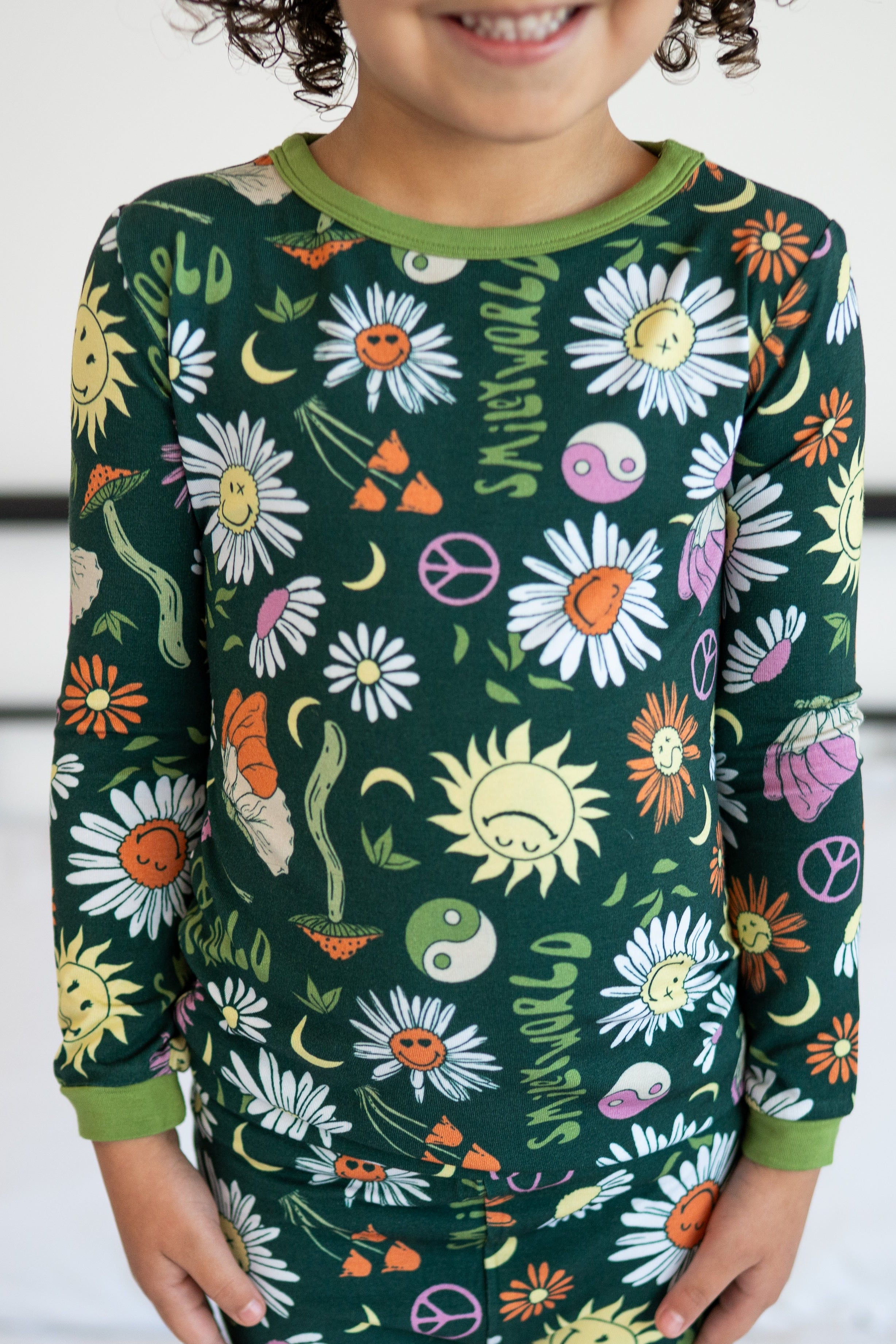 A child wears a green long-sleeved pajama top with a groovy floral SmileyWorld print.
