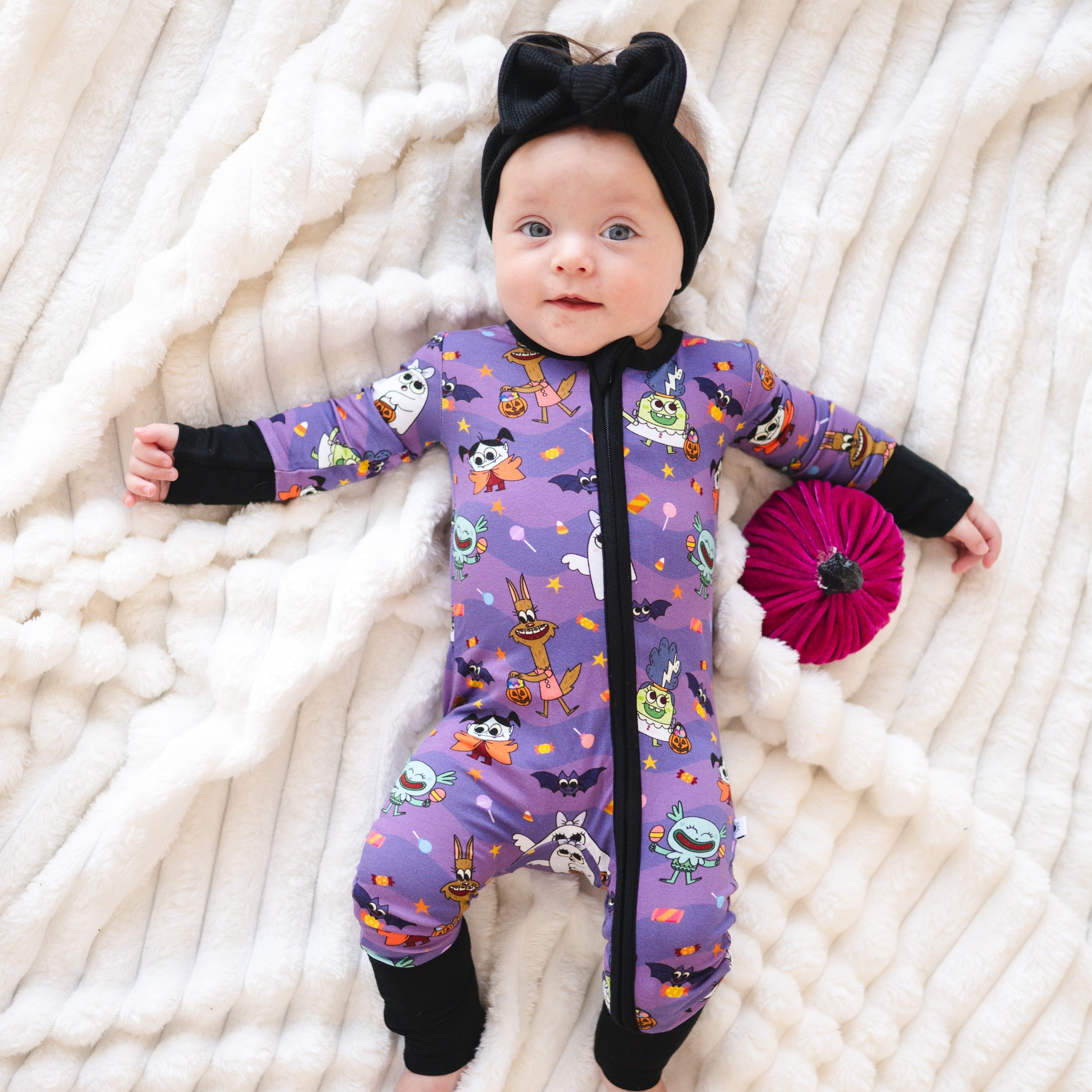 Baby in a purple monster party print bamboo zip pajama and black headband.