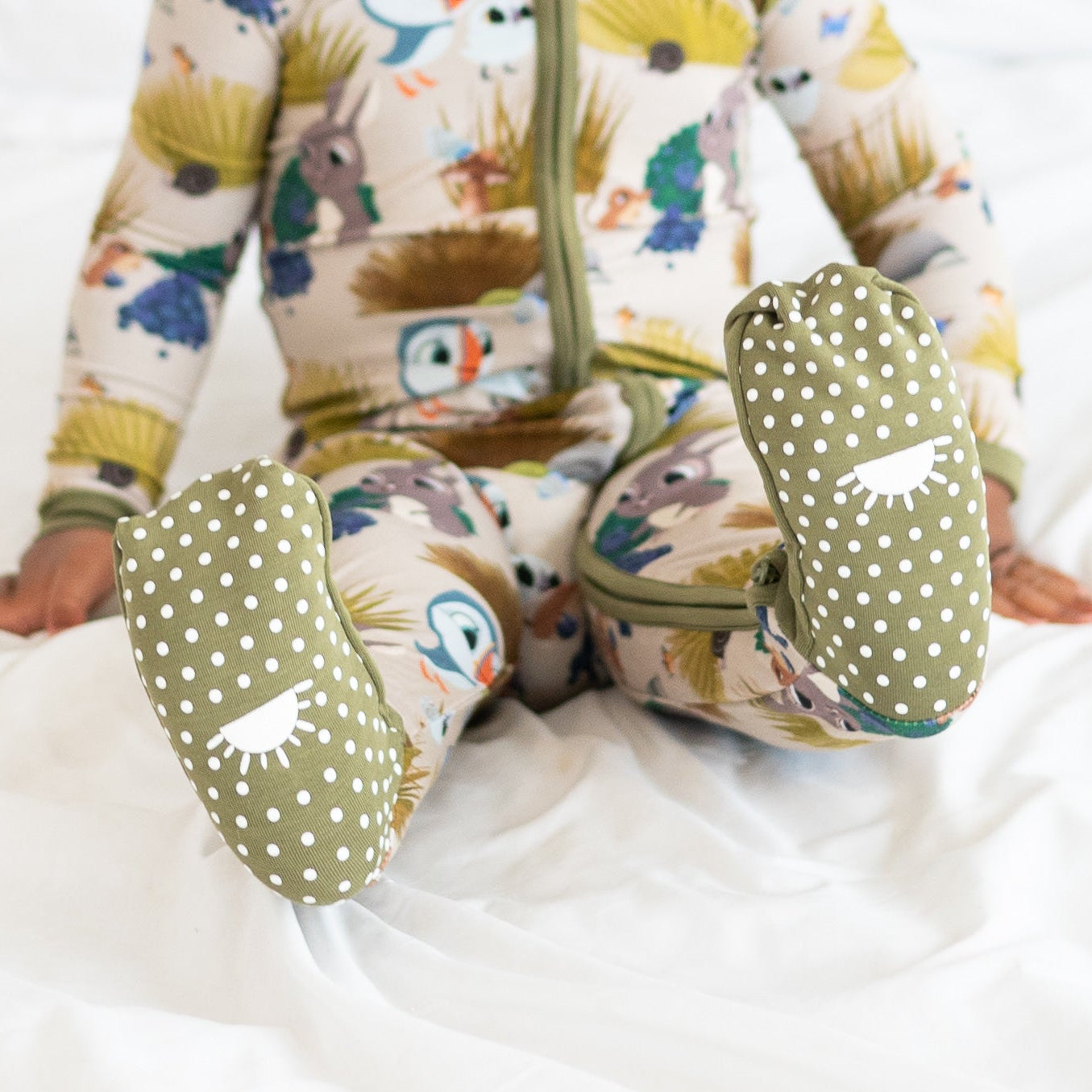 Baby in a Puffin Rock™ bamboo pajama with green polka dot footies.