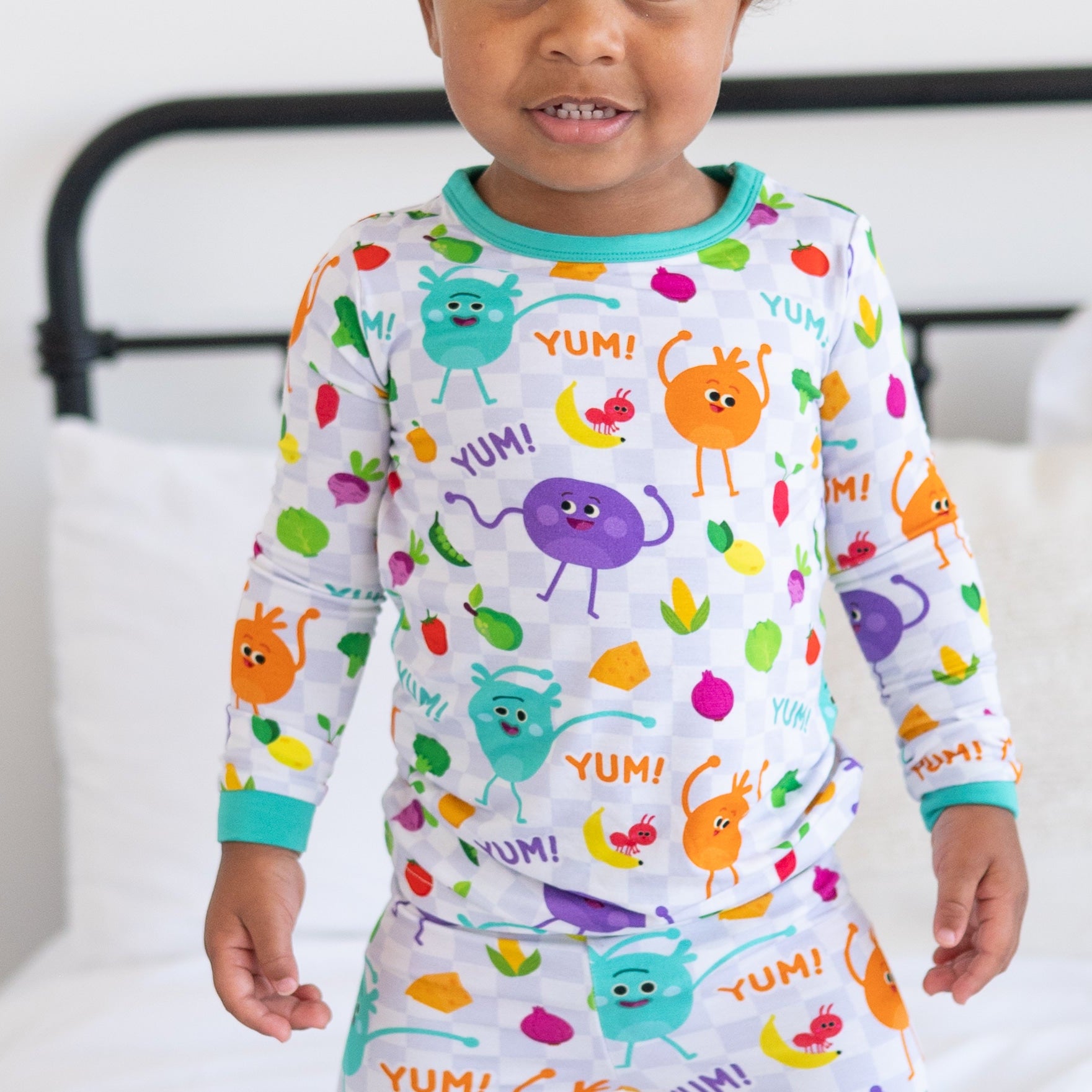 Toddler in long sleeve pajamas with a checkerboard pattern and cartoon vegetables.