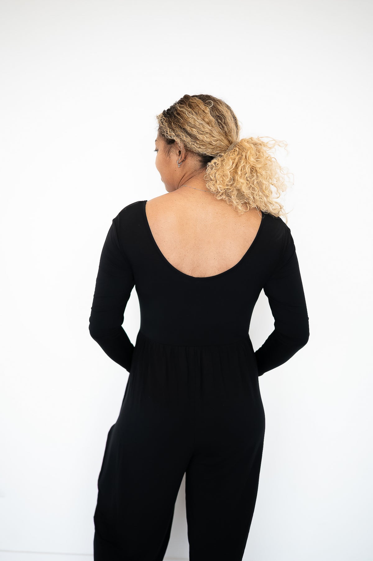 Rear view of a woman wearing a black long-sleeve romper with a deep scoop back.