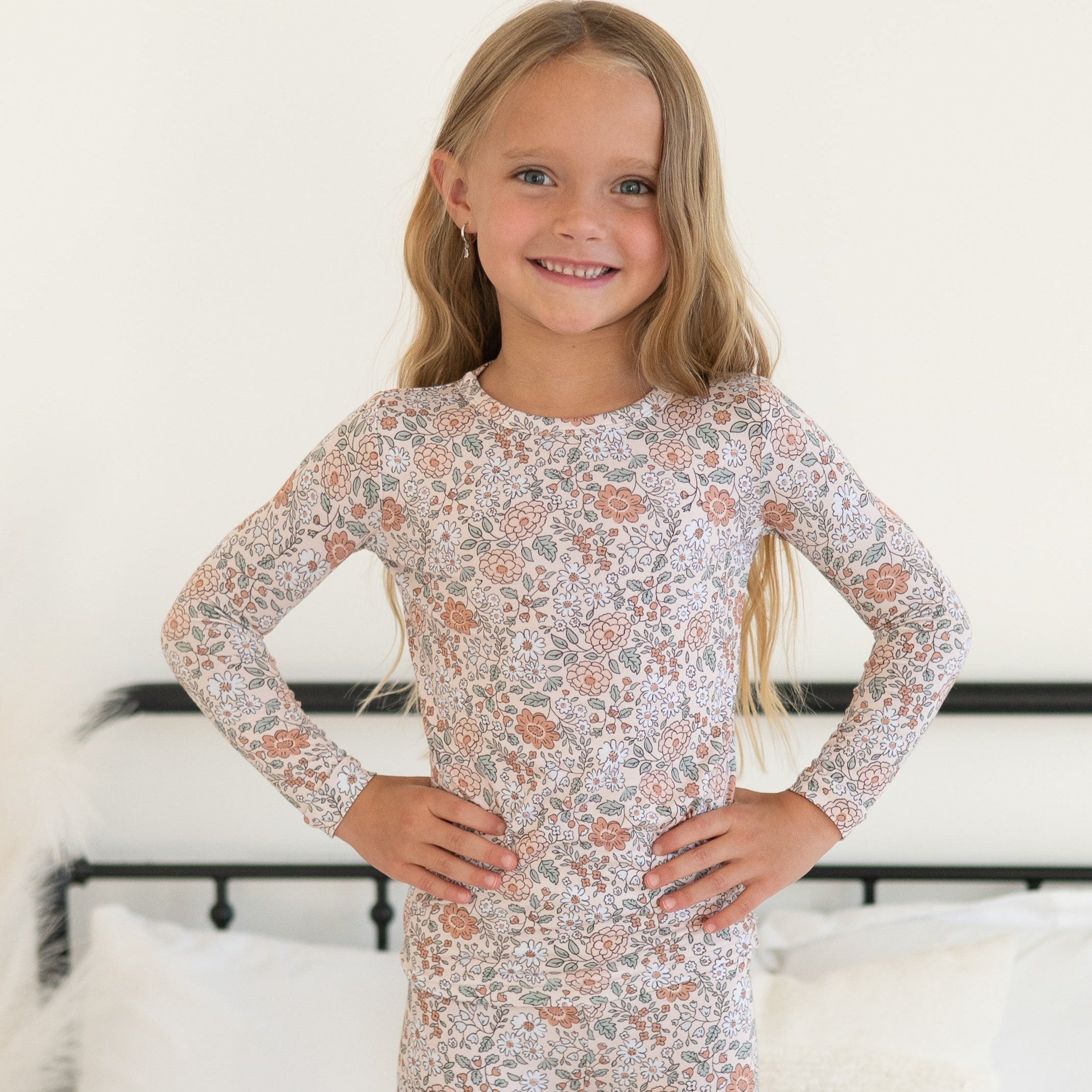A young girl smiles wearing a long-sleeved pajama set with a vintage floral print.