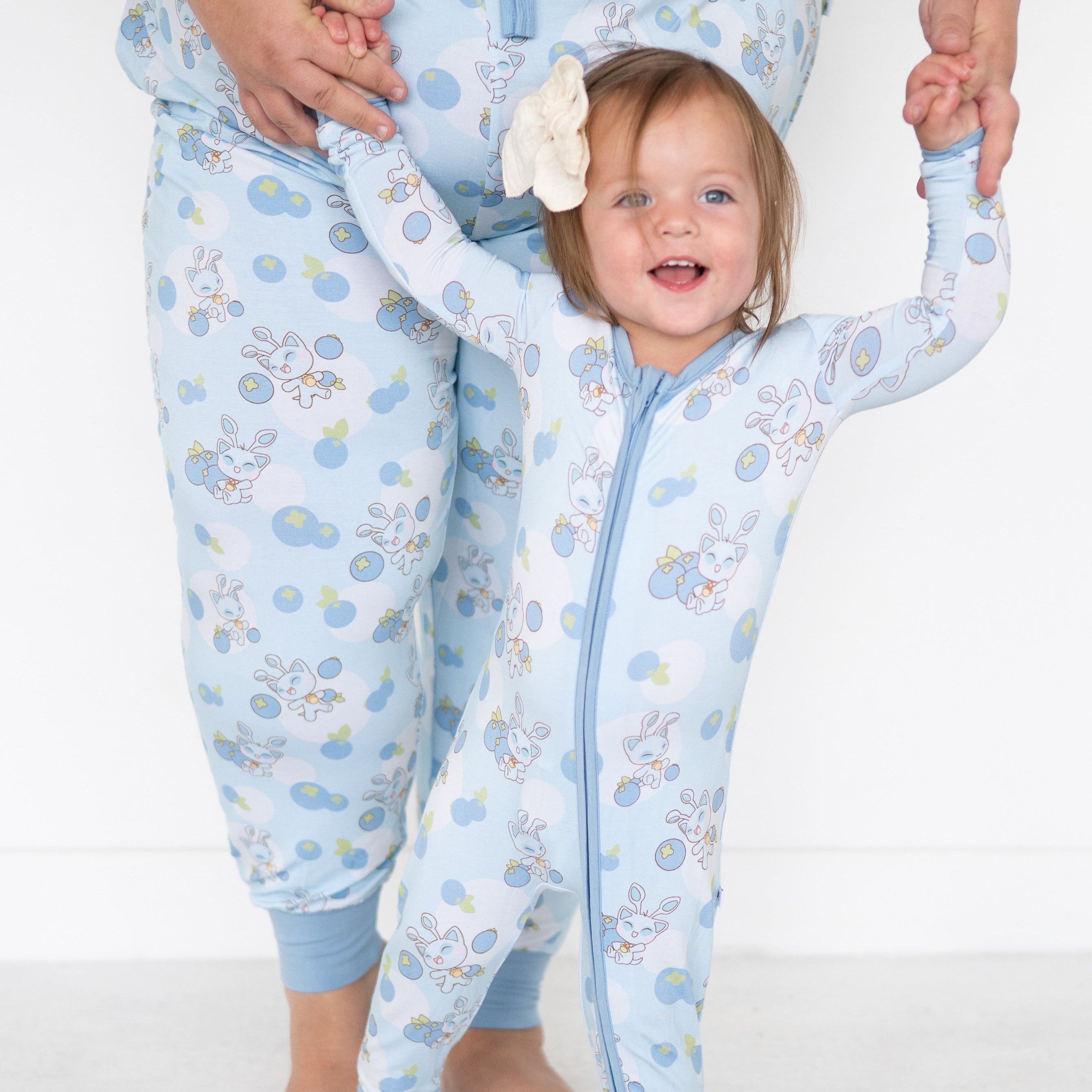 Baby in a light blue Neopets blueberry print zip-up pajama with a white bow.