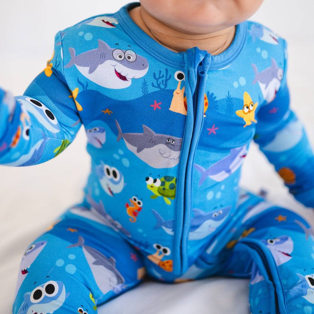 A baby wearing blue pajamas with a finny the baby shark print.
