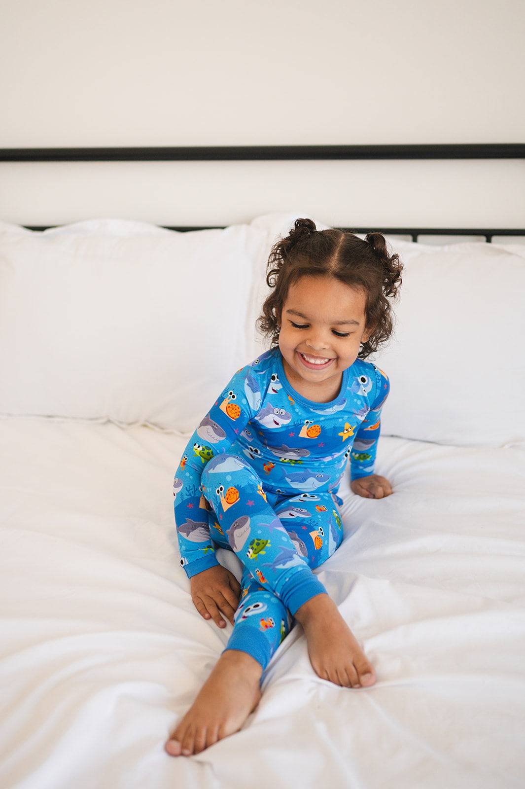 A young child smiles while wearing blue pajamas with a shark and sea creature print.