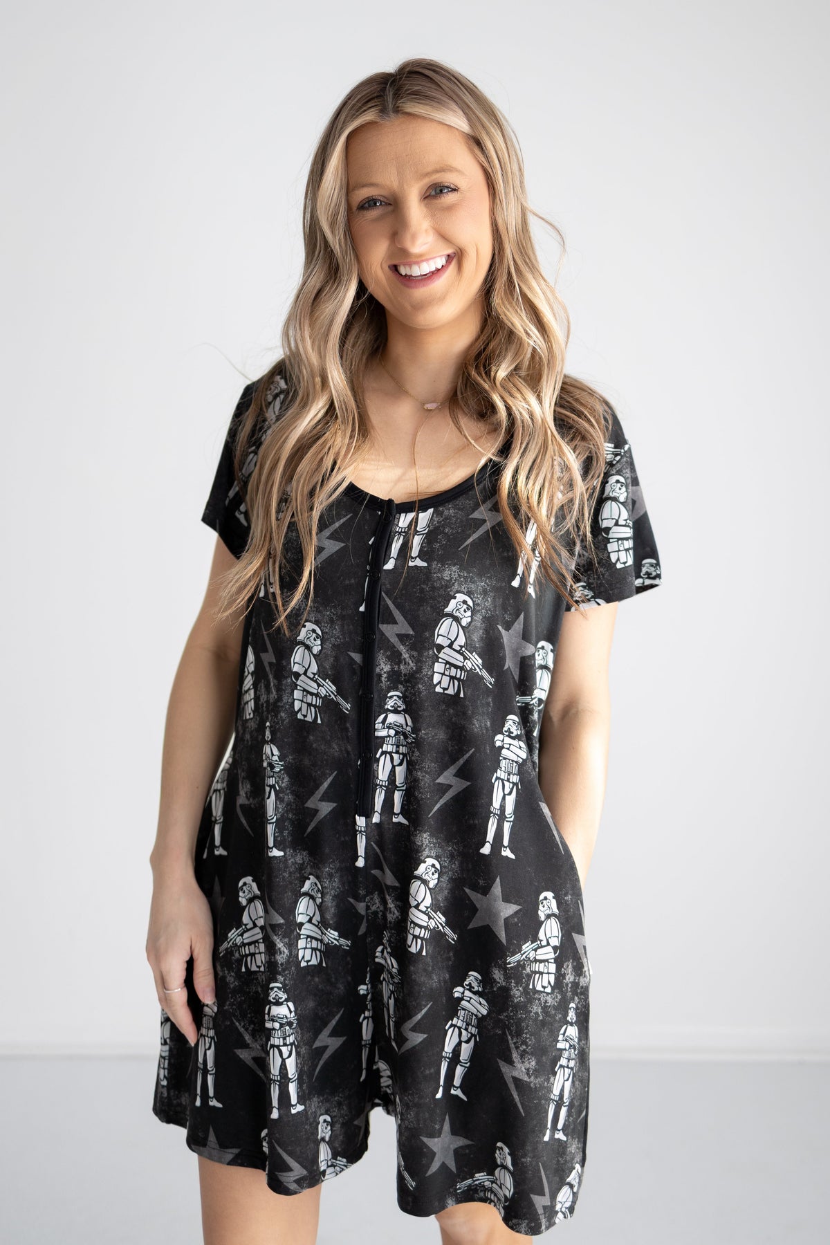 A woman smiles wearing a black shorty romper with a repeating pattern of white stormtroopers and stars.
