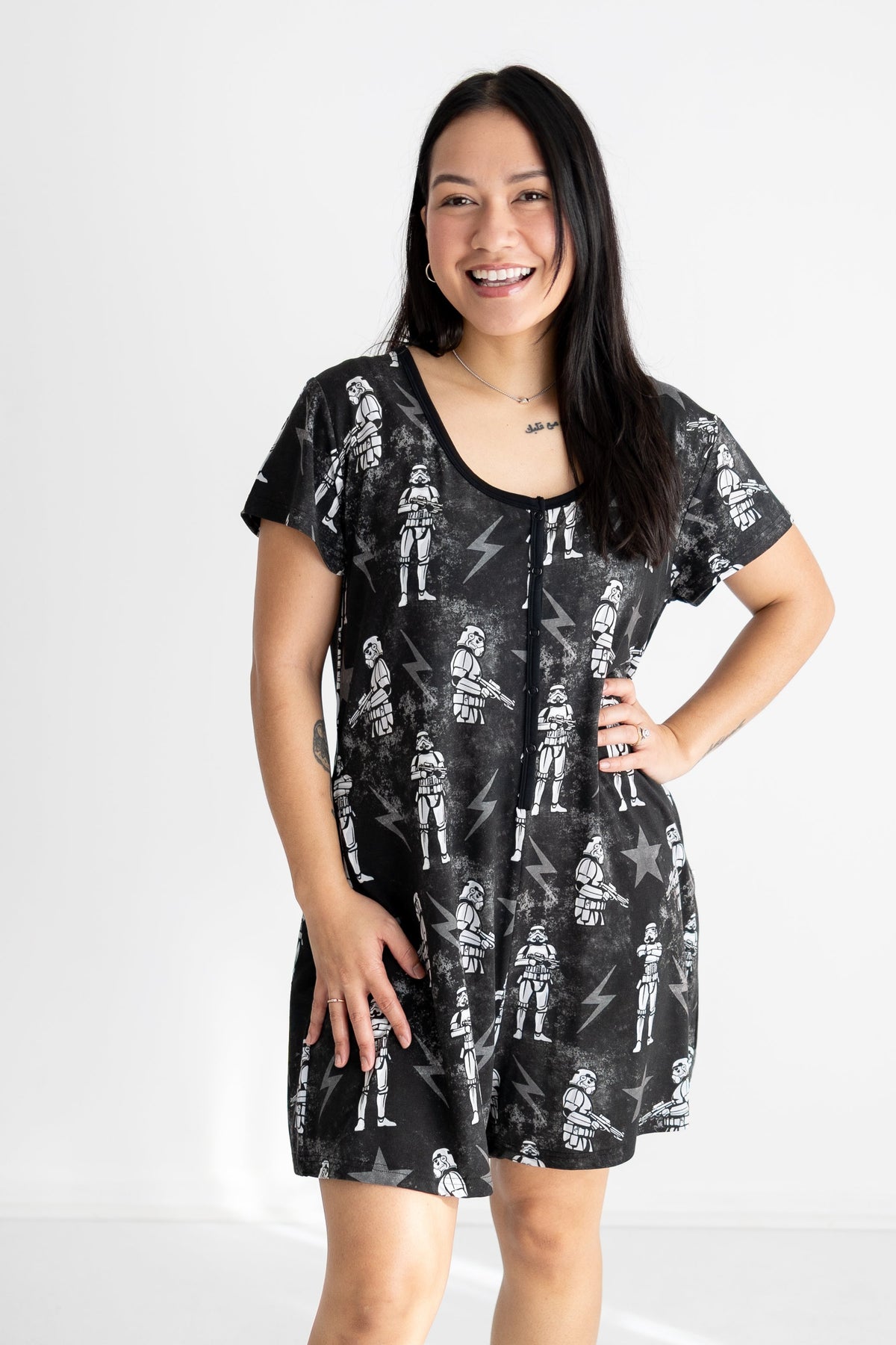 A woman smiles wearing a black shorty romper with a white stormtrooper and lightning bolt print.