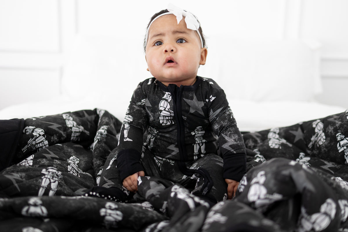 Baby in a black onesie with Stormtrooper print sits on a matching blanket.