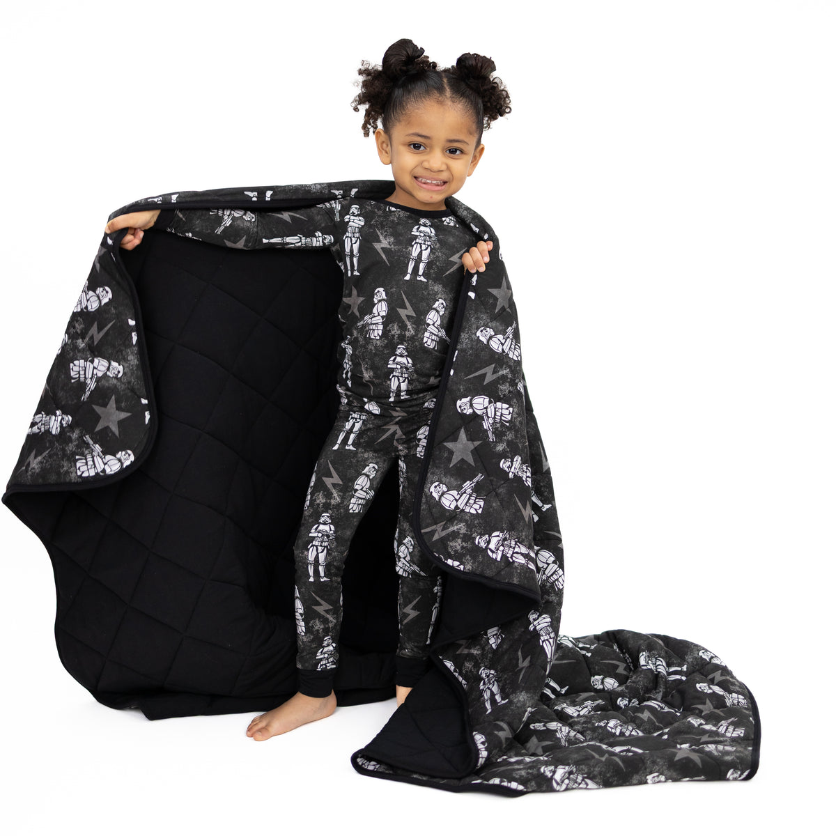 A young girl smiles while holding a black blanket with a stormtrooper print.