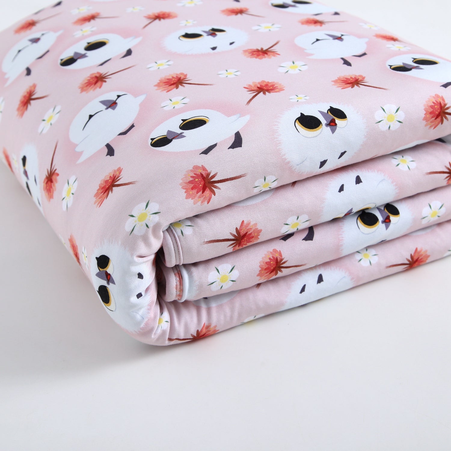 A pink blanket with a pattern of cartoon puffins and flowers.