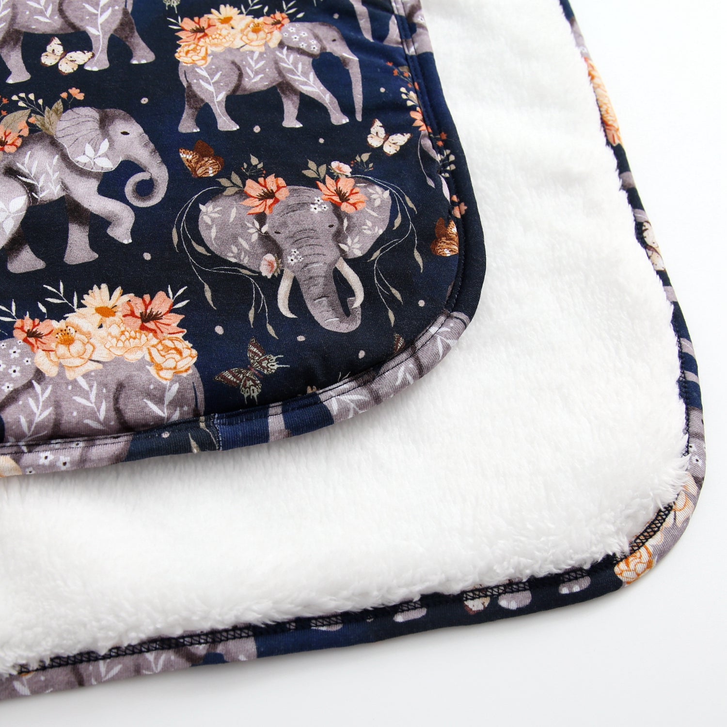 A plush blanket with a navy blue fabric featuring elephants and flowers, and a white plush underside.