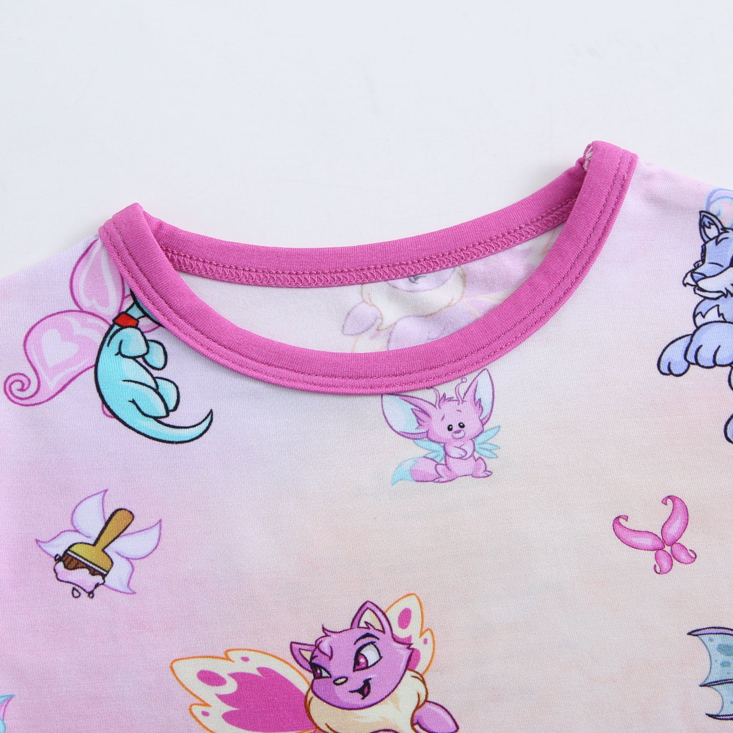 A light pink t-shirt with a pink neckline and a pattern of Neopets faeries.