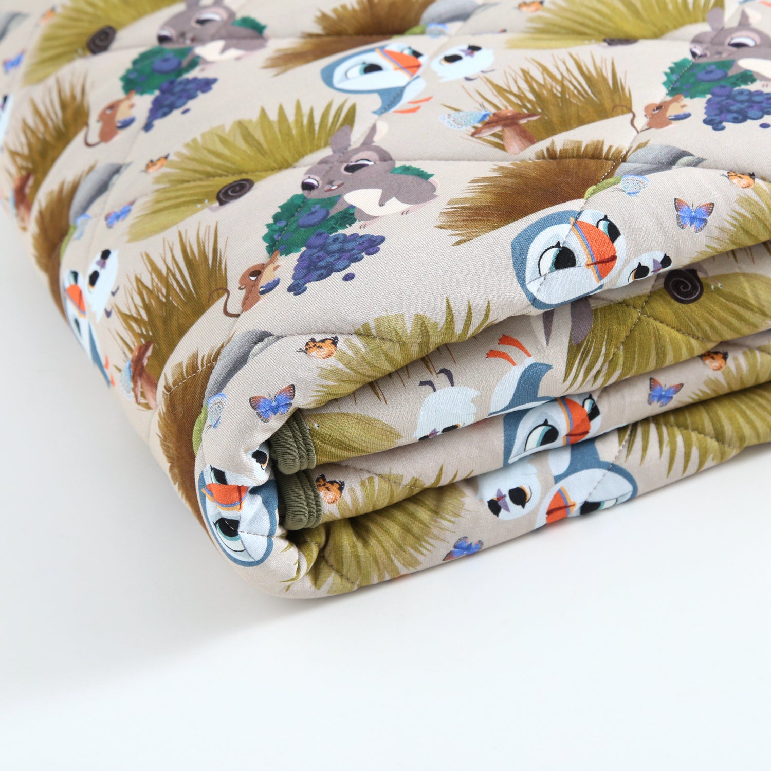 A folded quilted blanket with a Puffin Rock™ pattern featuring puffins, rabbits, and butterflies.