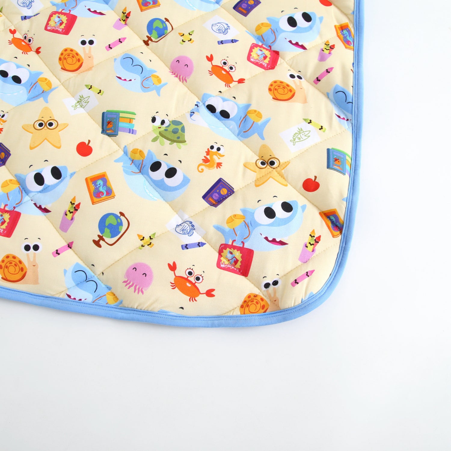 A light yellow quilted blanket with a pattern of cartoon sea creatures and school supplies.