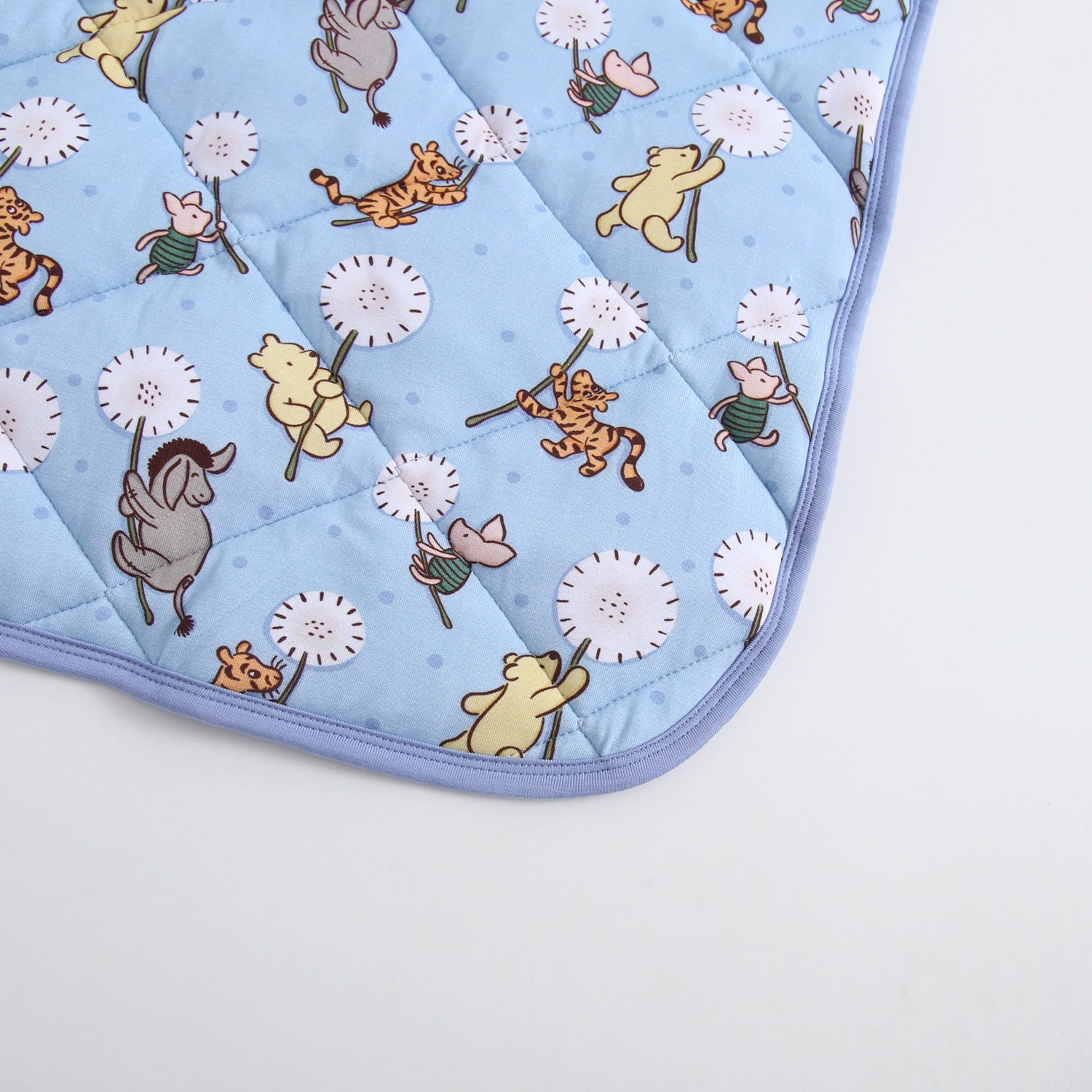 A light blue quilted blanket with a Winnie the Pooh and friends dandelion print.