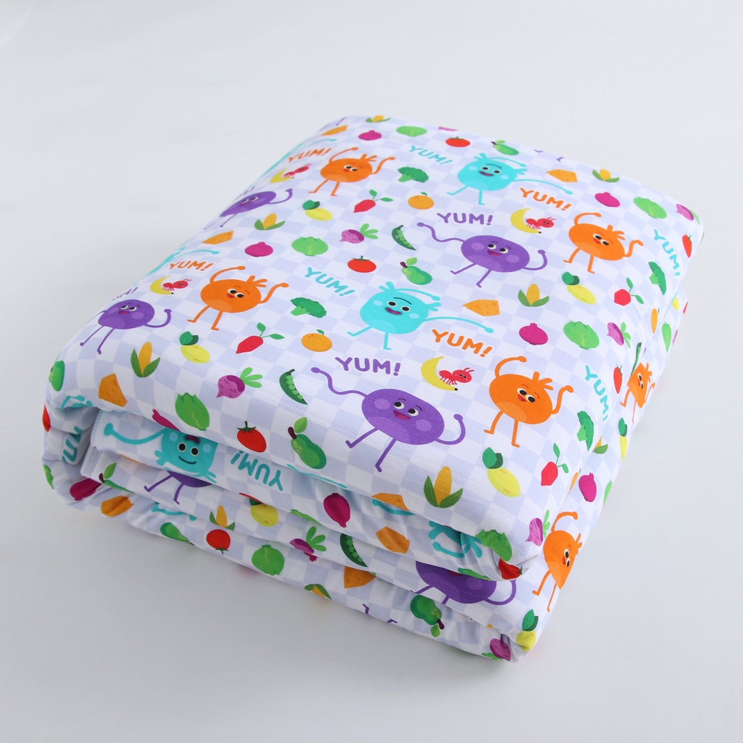 A folded blanket with a pattern of cartoon fruits and vegetables saying "YUM!".