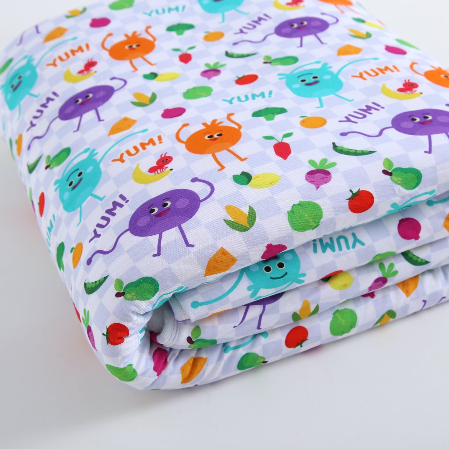 A folded blanket with a playful pattern of cartoon vegetables and characters saying "YUM!".